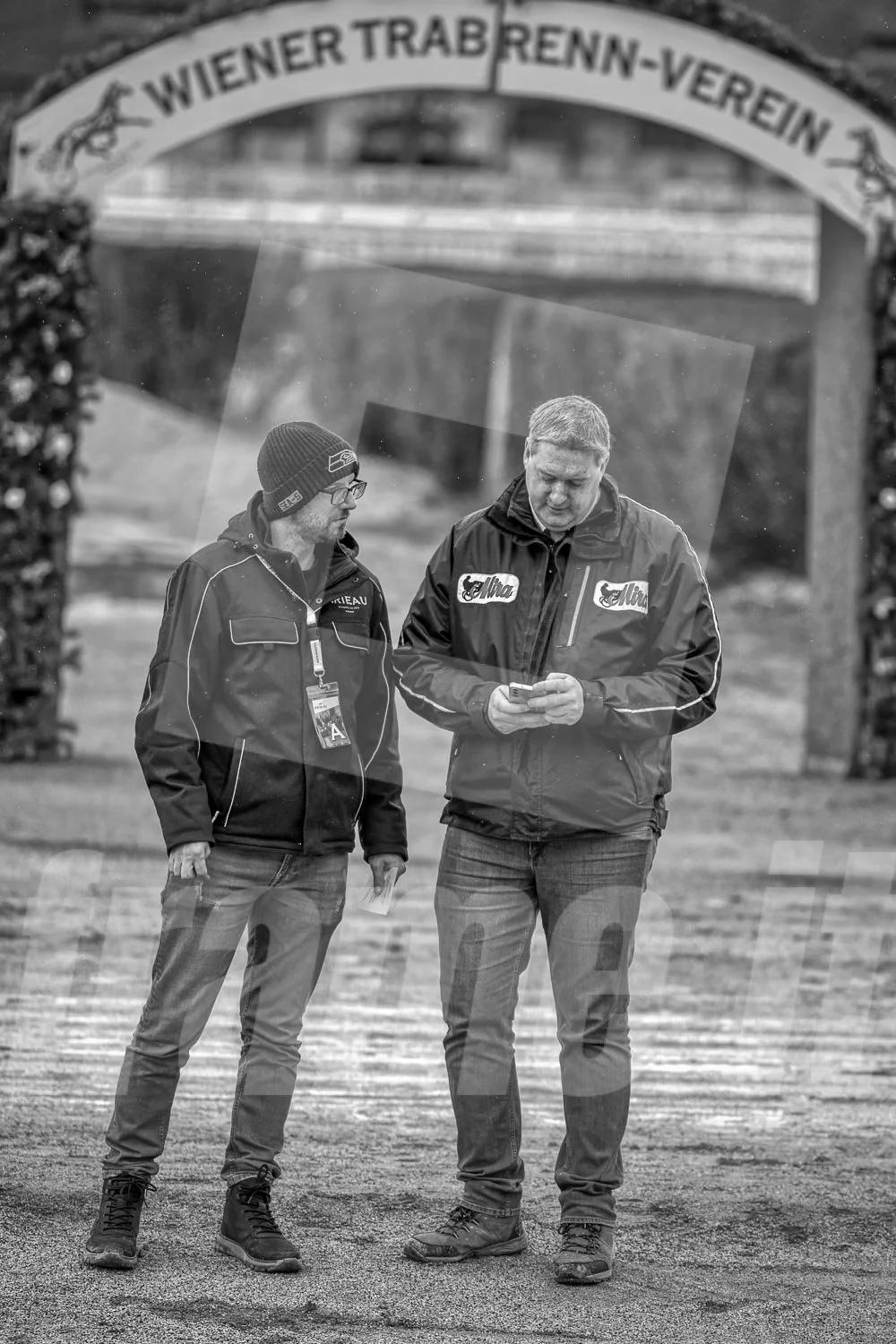 Zwei Männer unter einem Torbogen mit der Aufschrift 'Wiener Trab Renn-Verein'.