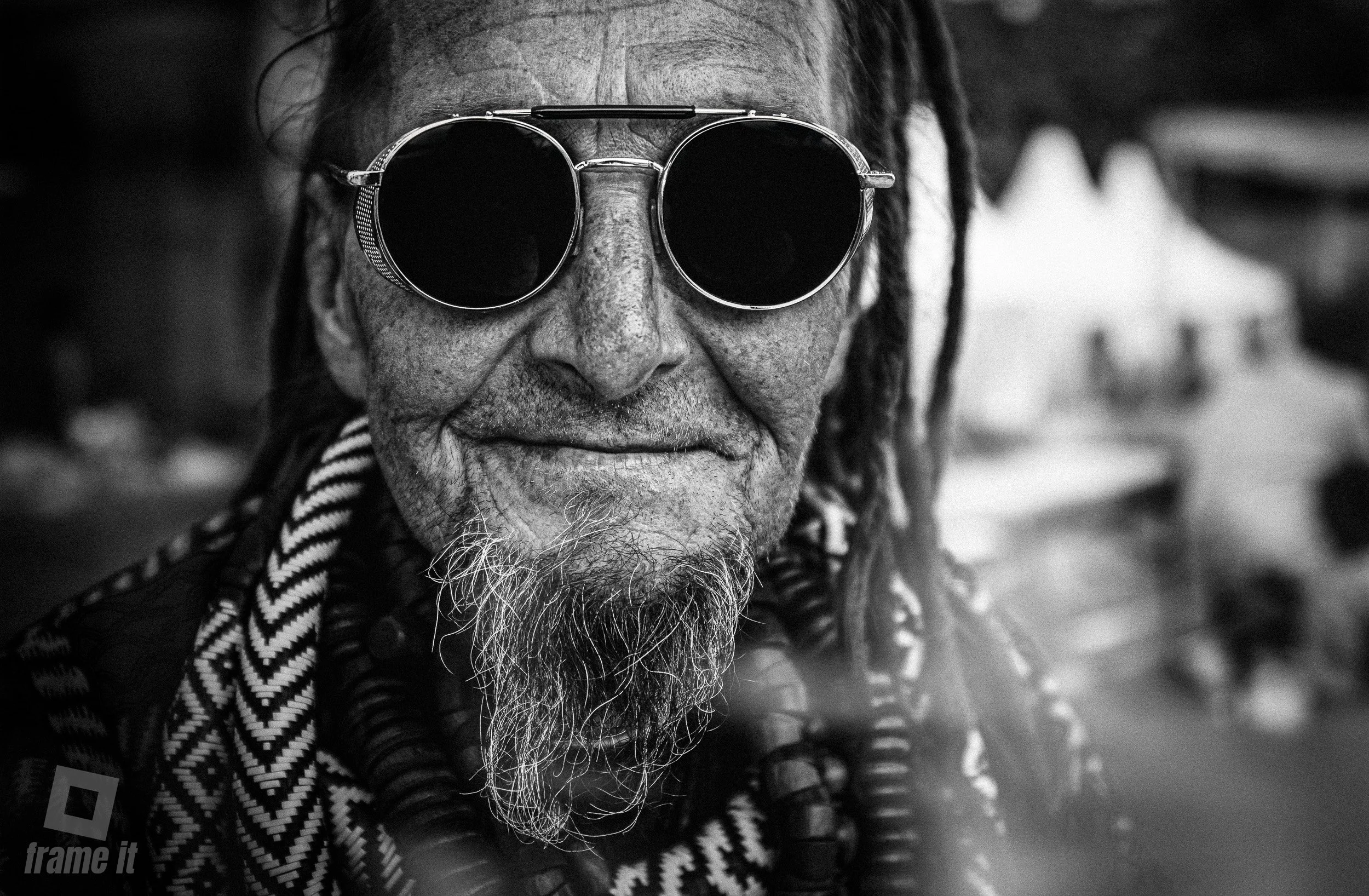 Ein älterer Mann mit Dreadlocks, großer Sonnenbrille und sichtbarem Gesicht. Er trägt Schmuck und ein Musterndes Kleidungsstück, aufgenommen auf den Afrika Tagen in Wien. Das Bild ist schwarz-weiß.