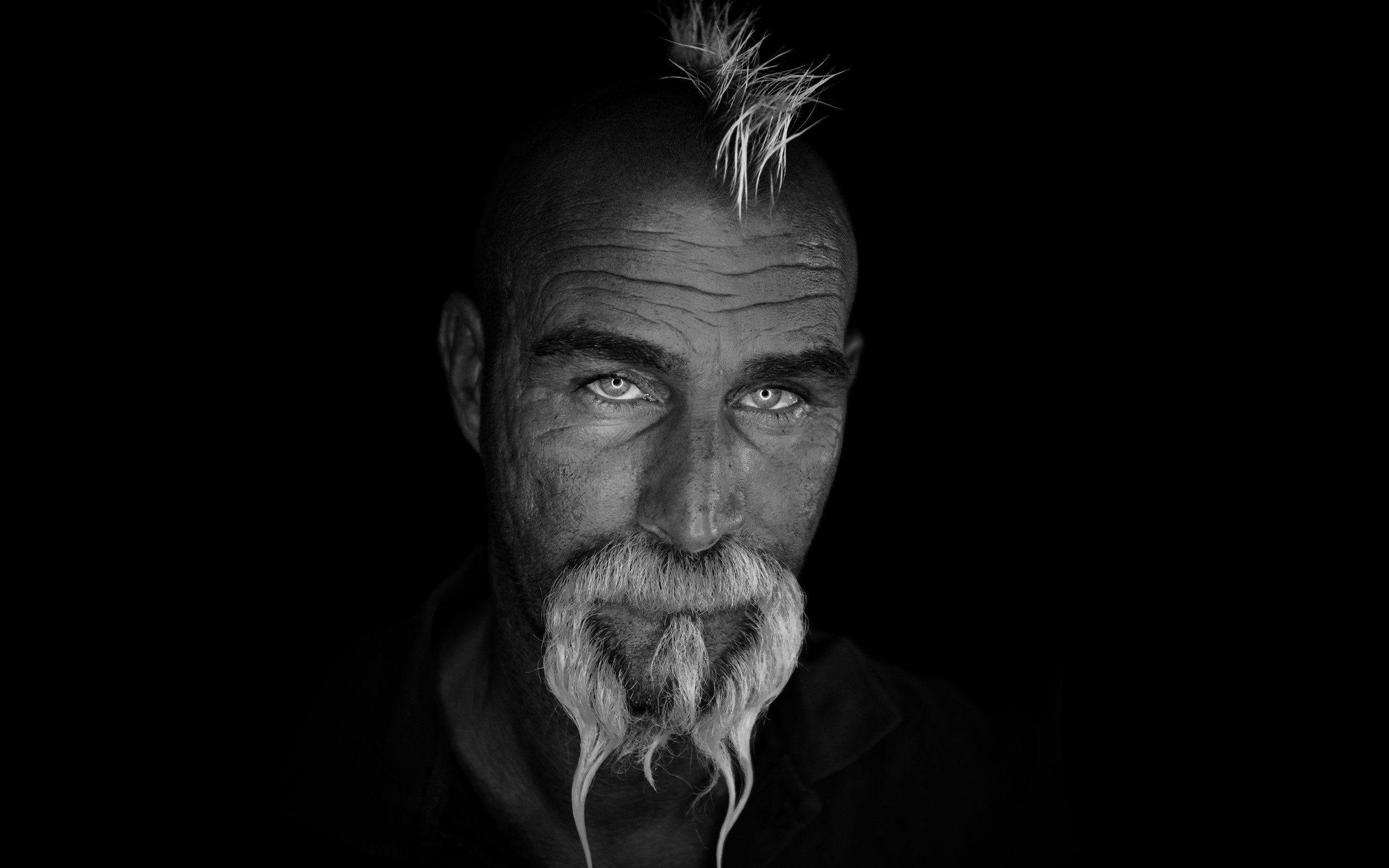 Schwarz-weiß Porträt eines älteren Mannes mit weißen Haaren und Bart, auf schwarzem Hintergrund.