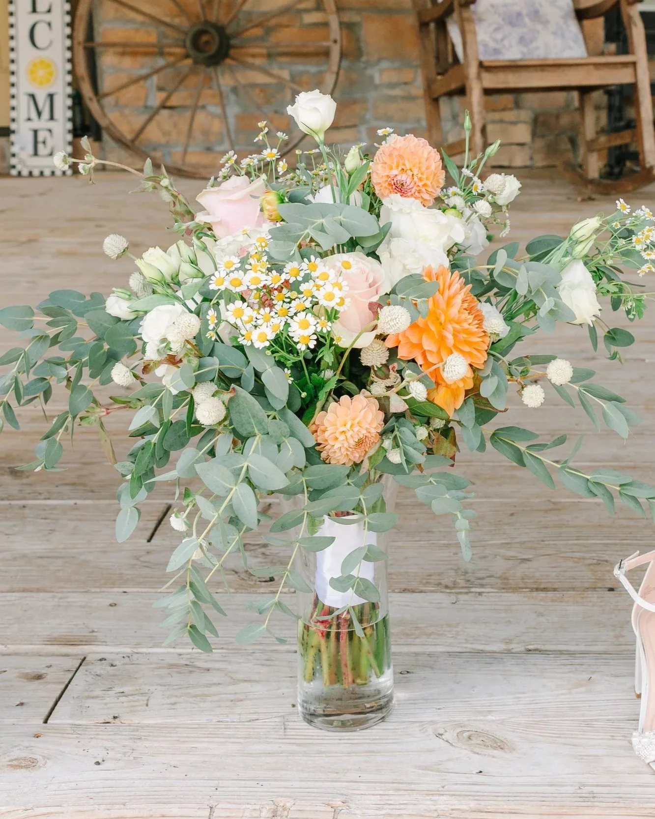 A colorful bouquet of flowers in a tall glass vase on a wooden table with a rustic decor background.