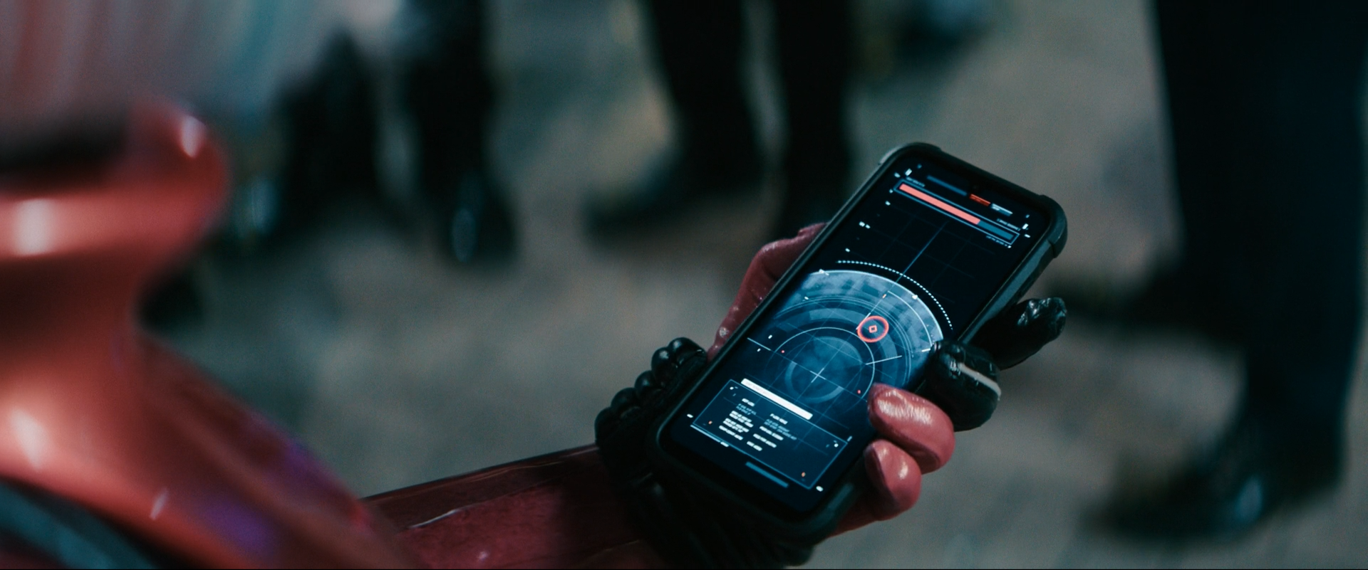 A person wearing gloves is holding a smartphone displaying a futuristic targeting or scanning interface with a radar-like graphic and data metrics.