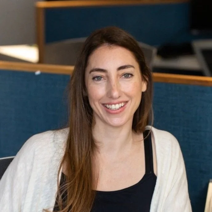 Smiling woman with long brown hair sitting in an office cubicle.