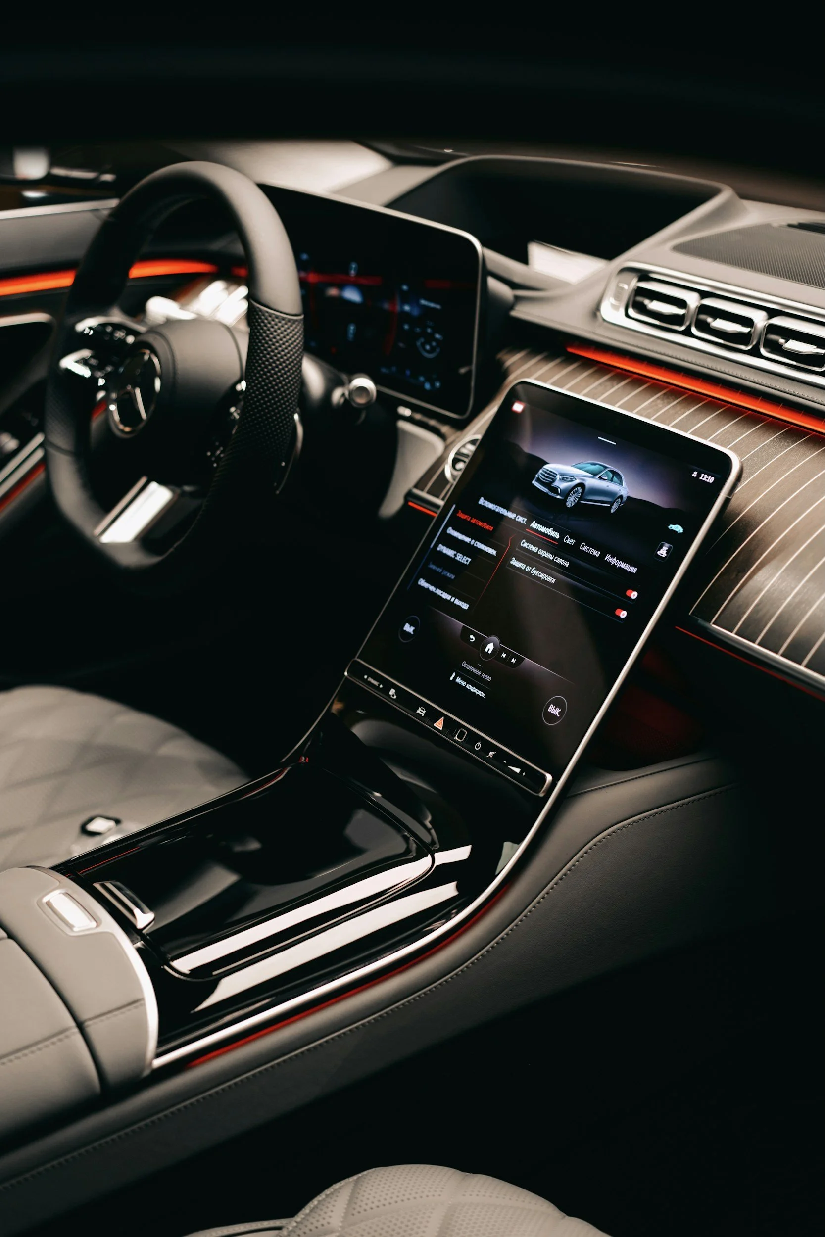 The interior of a luxury car showing a digital dashboard, steering wheel, touchscreen display with a car image, and stylish interior design with red accents and leather seats.