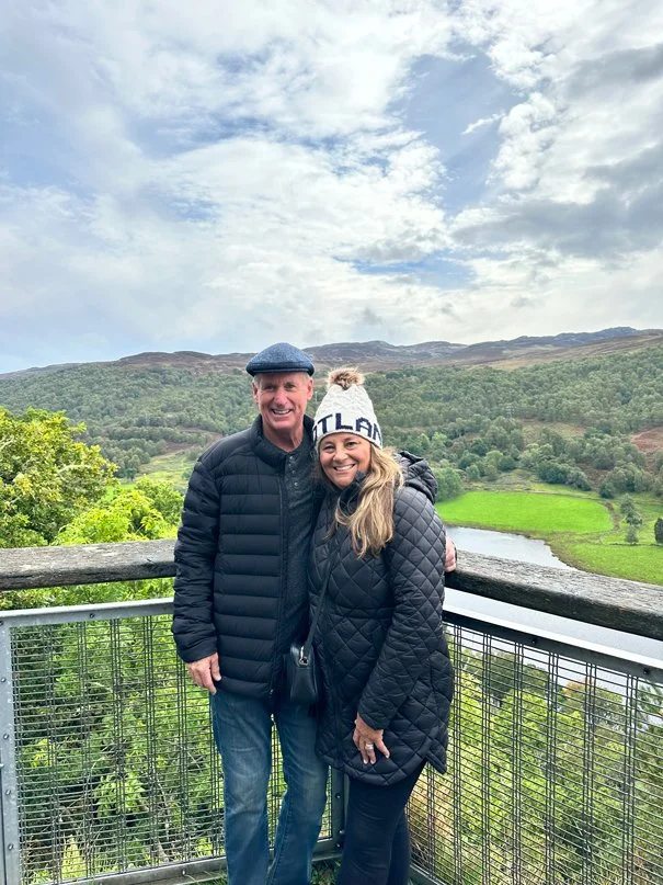 Man and woman standing on a deck on a cloudy day with a river running behind them.