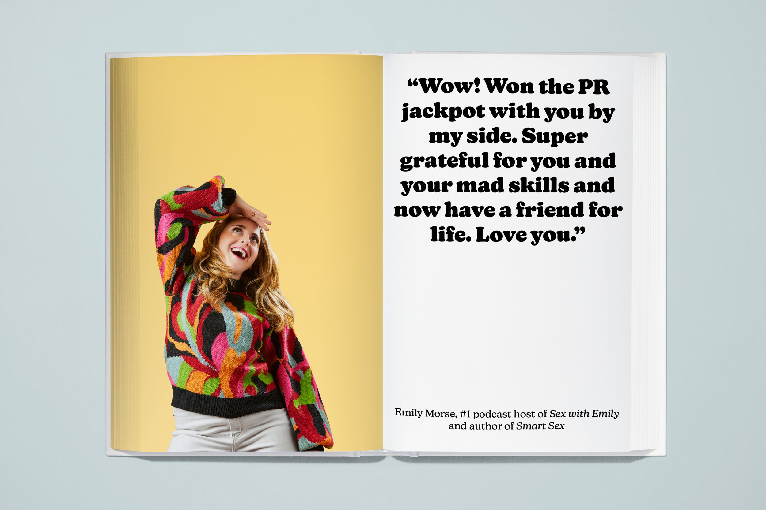An open book with a photograph of a woman wearing a colorful patterned sweater, smiling and holding her hand to her forehead, on a yellow background. The right page has a quote from Emily Morse, praising her for winning a PR jackpot and becoming a go