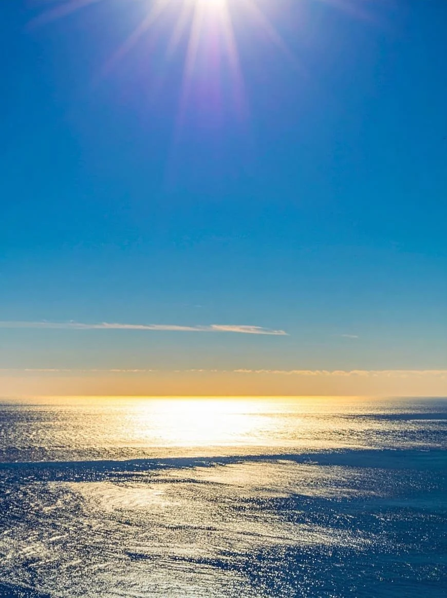 Sun shining brightly over the ocean with a clear blue sky and shimmering water.