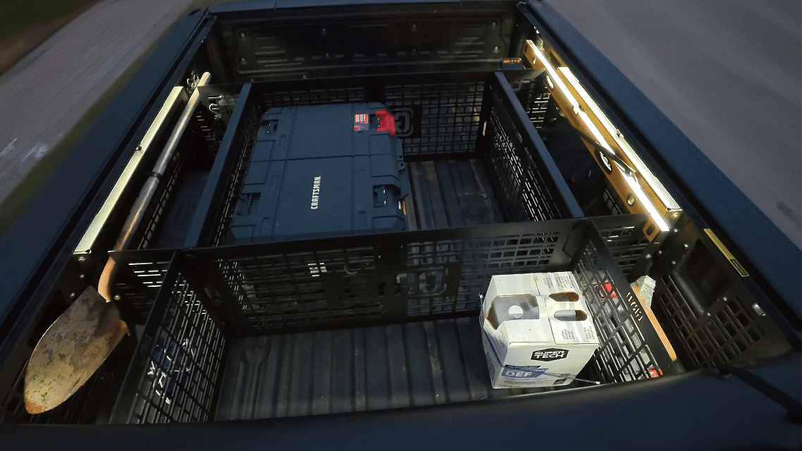 View inside the bed of a pickup truck with organized crates and tools, including a toolbox and a box of beverages.