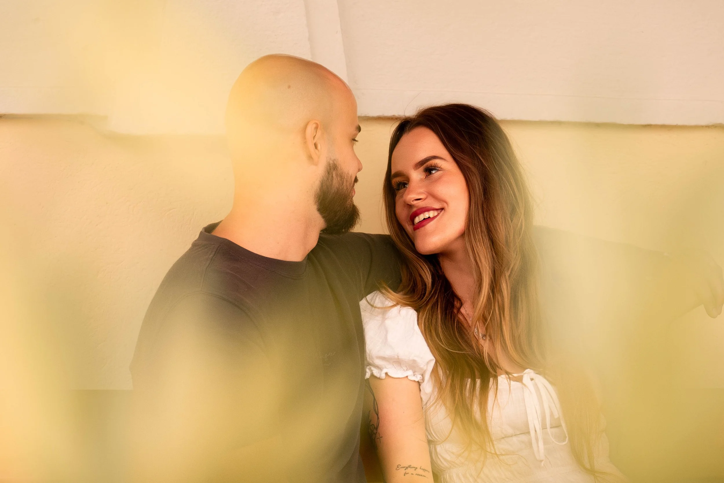 A man and woman sit close together, gazing into each other's eyes and smiling warmly.