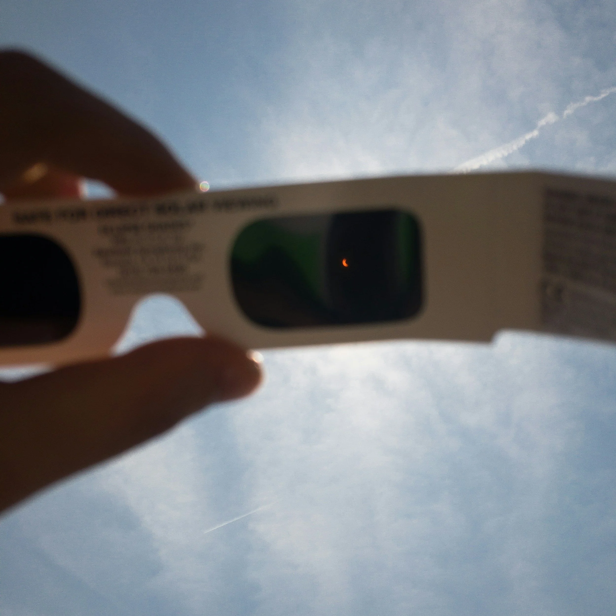 A person holding a box of contact lenses or eye care product against a clear blue sky with a few contrails.