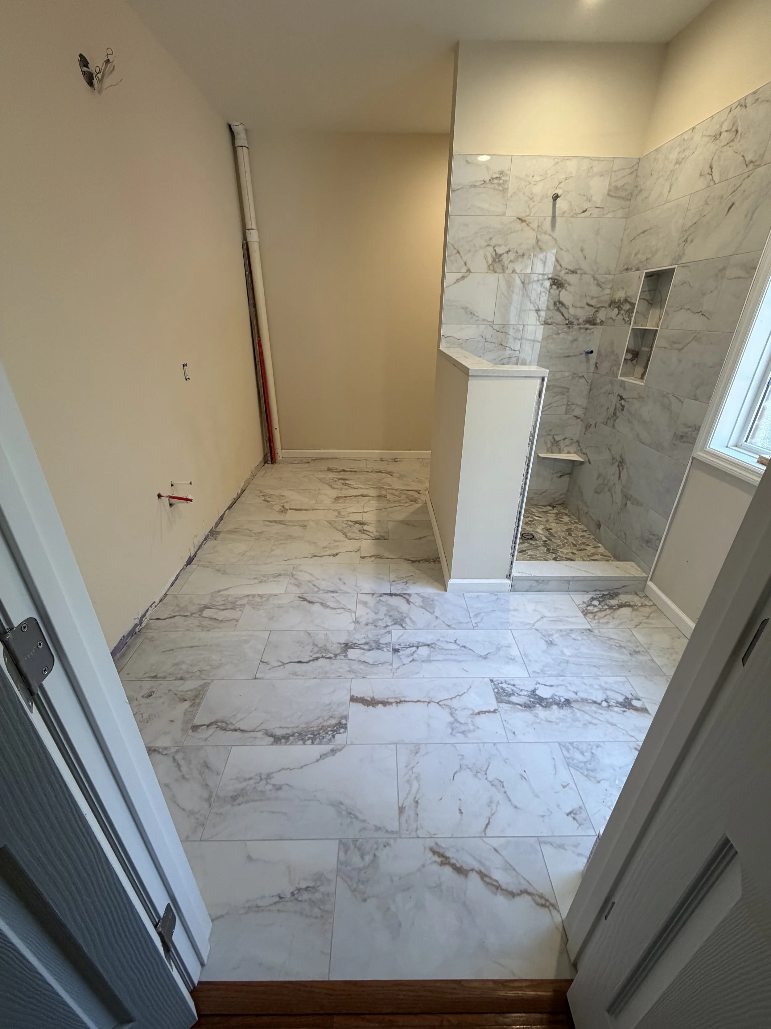 Bathroom under construction with marble tiles on the floor and shower walls, and plumbing fixtures not yet installed.