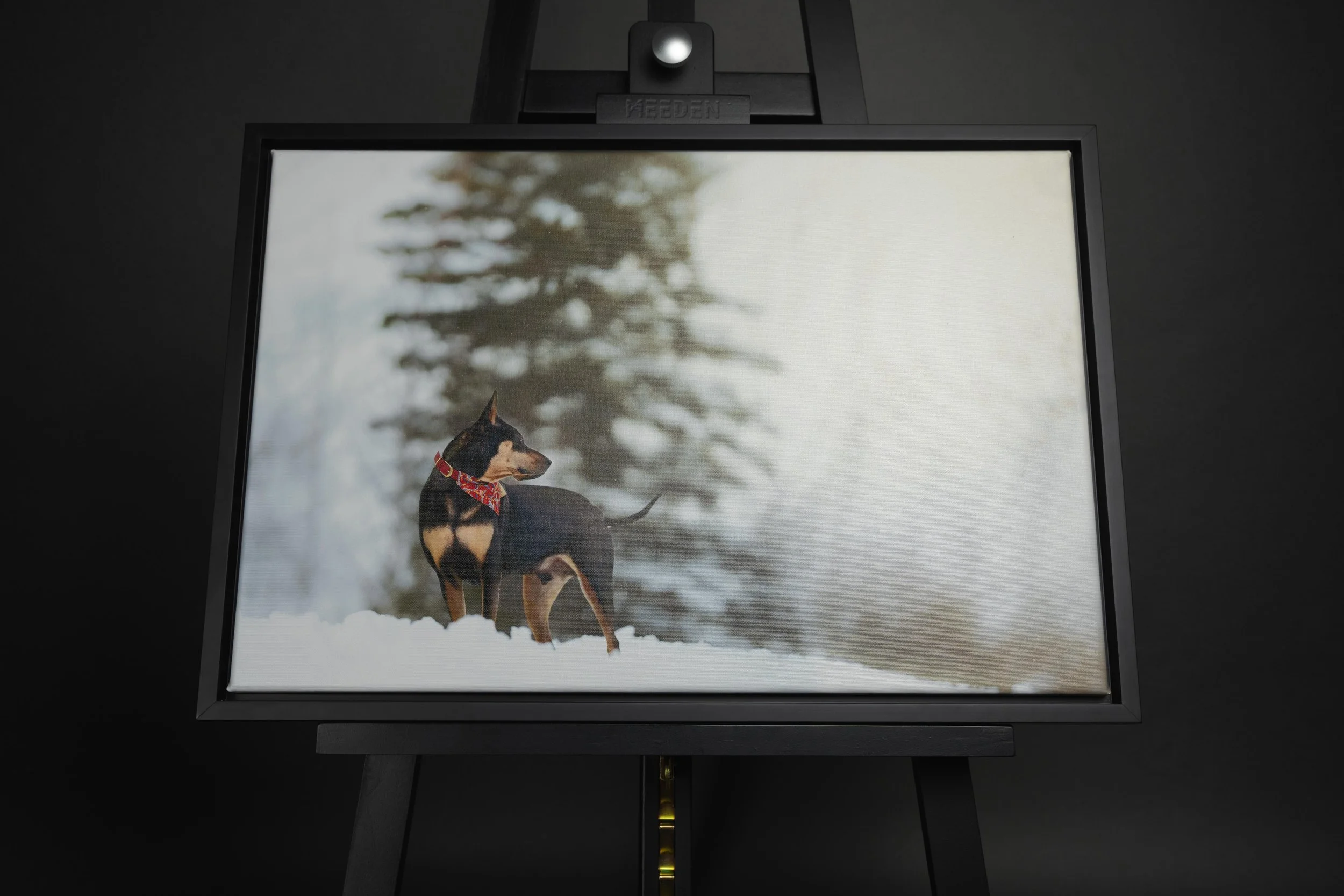 A framed photograph of a dog standing in snow with a blurred tree in the background.