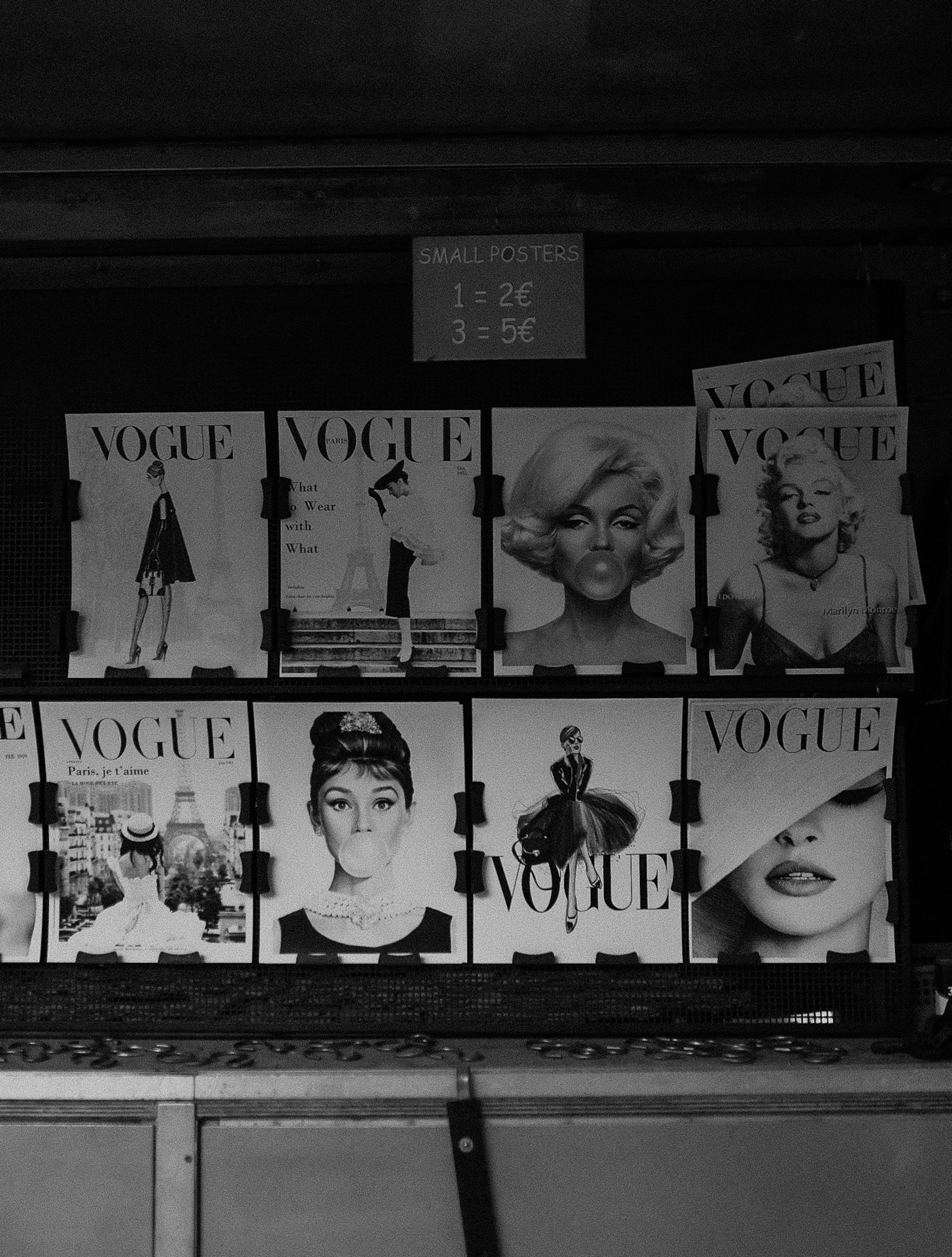 Display of vintage Vogue magazine covers featuring iconic models, arranged on a stand with a sign above advertising small posters for €2 and €5.