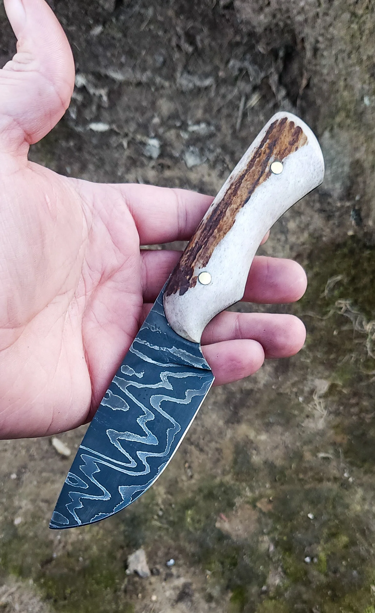 A person holding a knife with a patterned metal blade and a handle made from antler.