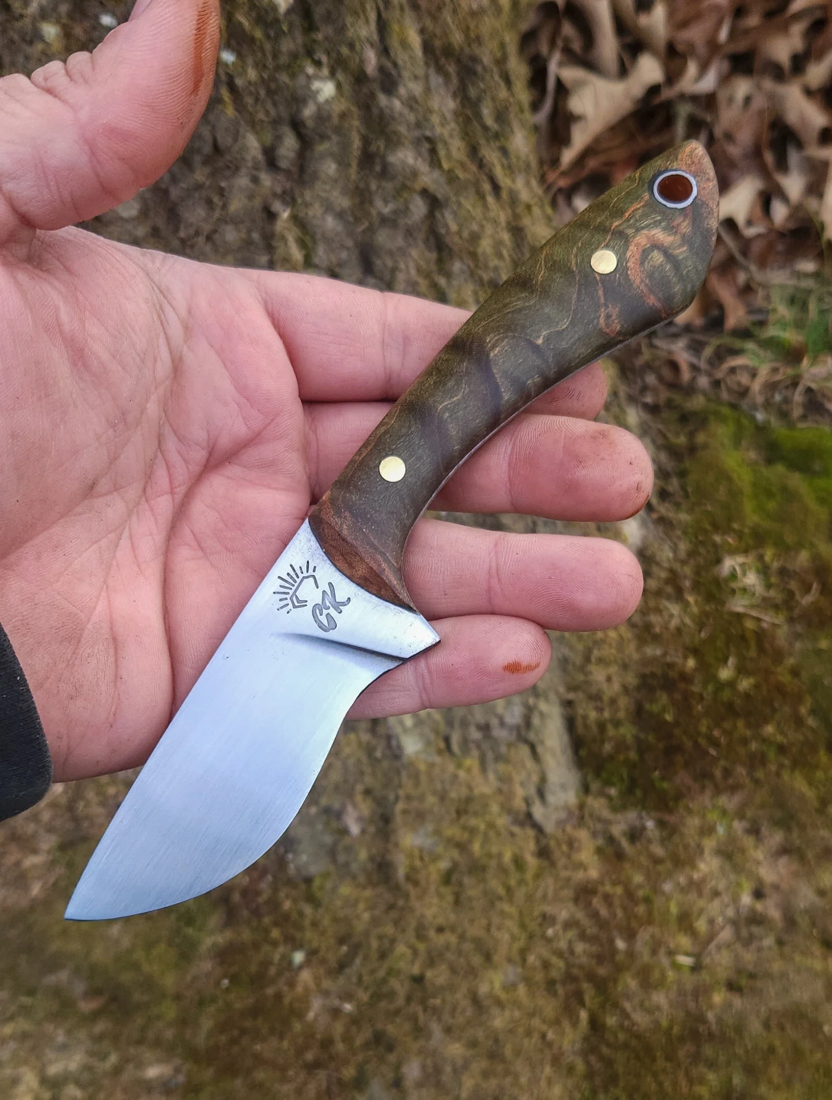 Hand holding a small fixed-blade knife with a wooden handle and a stainless steel blade with branding.