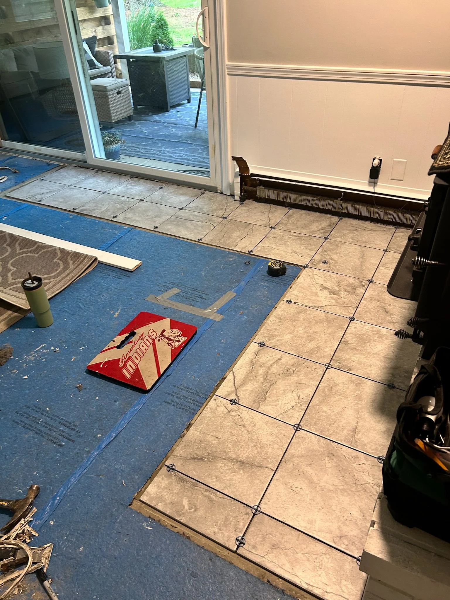 Kitchen floor renovation in progress with partially installed beige marble tiles and blue underlayment. 