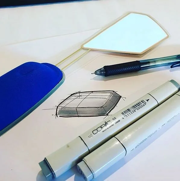 Sketch of a 3D rectangular object with three facing perspectives, along with a black pen, a white marker, a blue mouse pad, and a mirror on a white surface.
