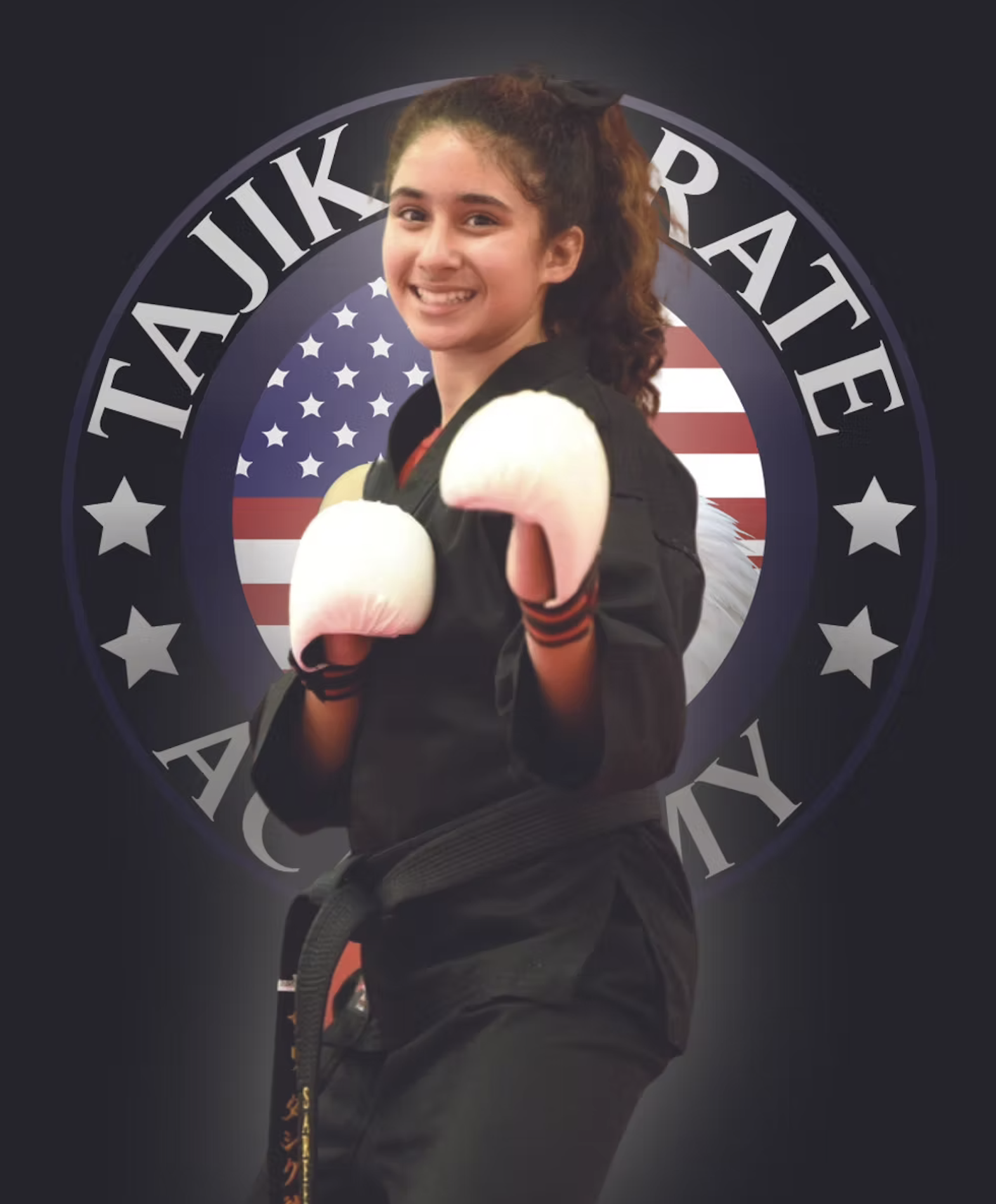 Young female martial artist in black uniform with white gloves, posing with fists raised, smiling, standing in front of a logo with American flag and stars.