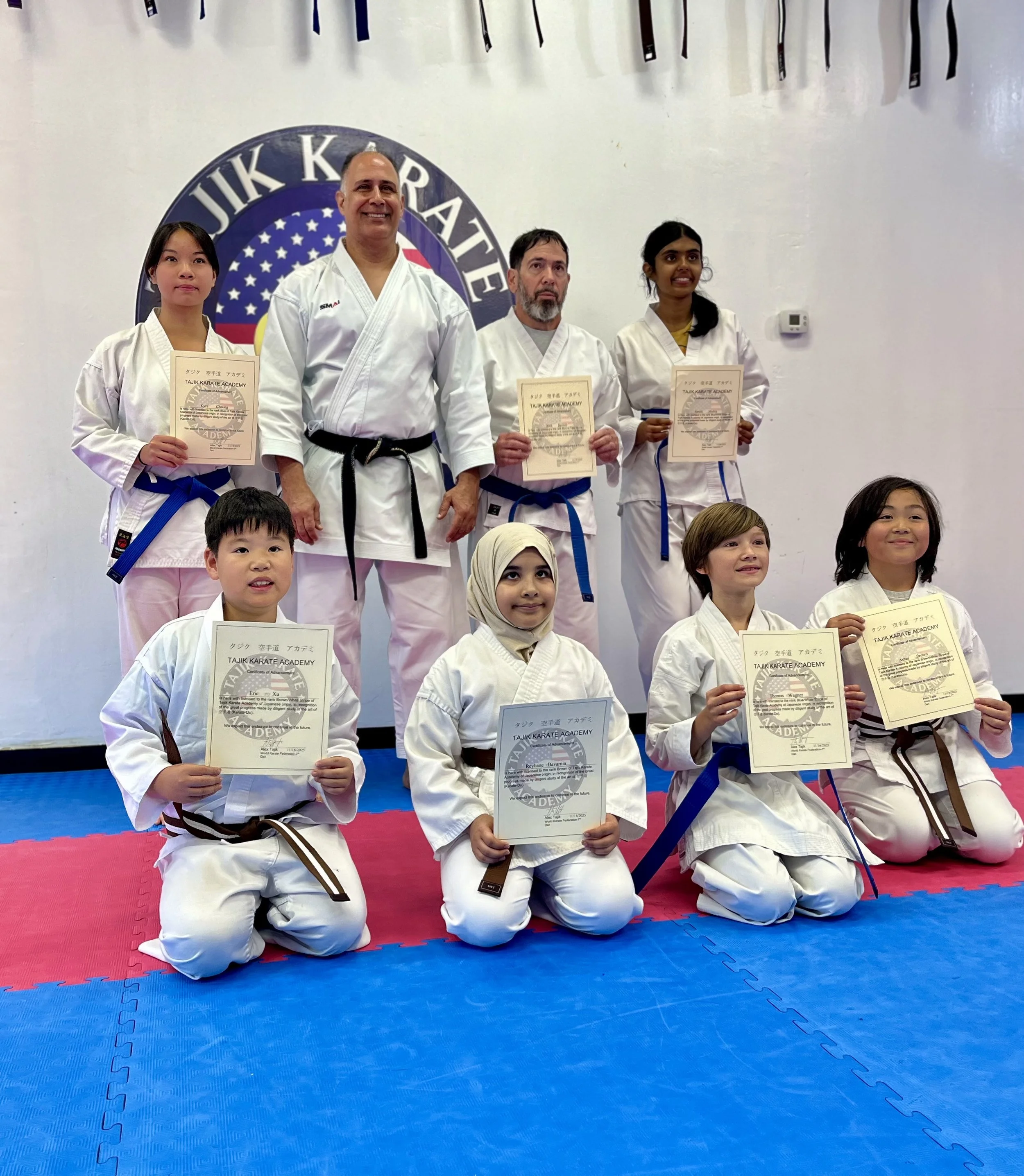 Group of children and instructors in martial arts uniforms posing with certificates in a dojo.