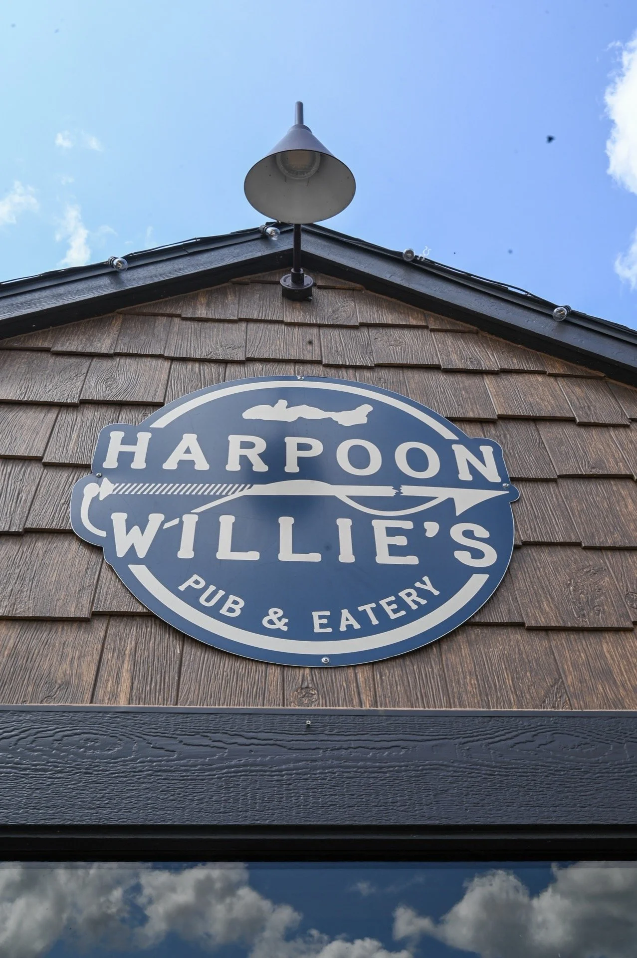Sign for Harpoon Willie's Pub & Eatery on a wooden building, with a light fixture above and a partly cloudy sky in the background.