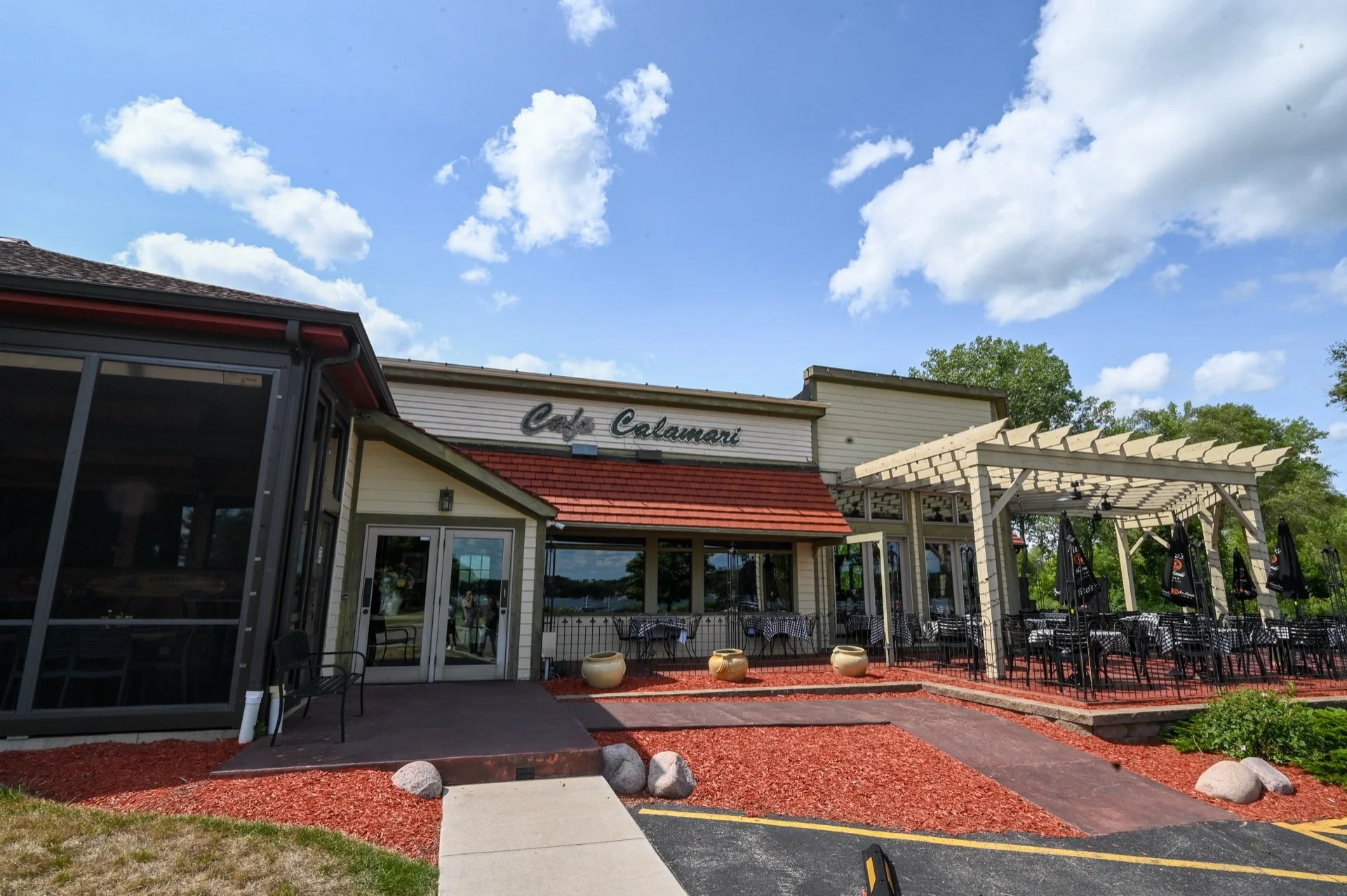 Exterior of a restaurant named Caffé Celamari with outdoor seating area, a pergola, and a clear blue sky with clouds.