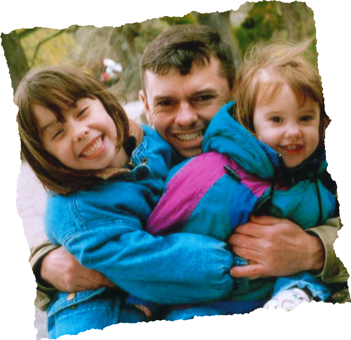 A man hugging two young children outdoors, all smiling
