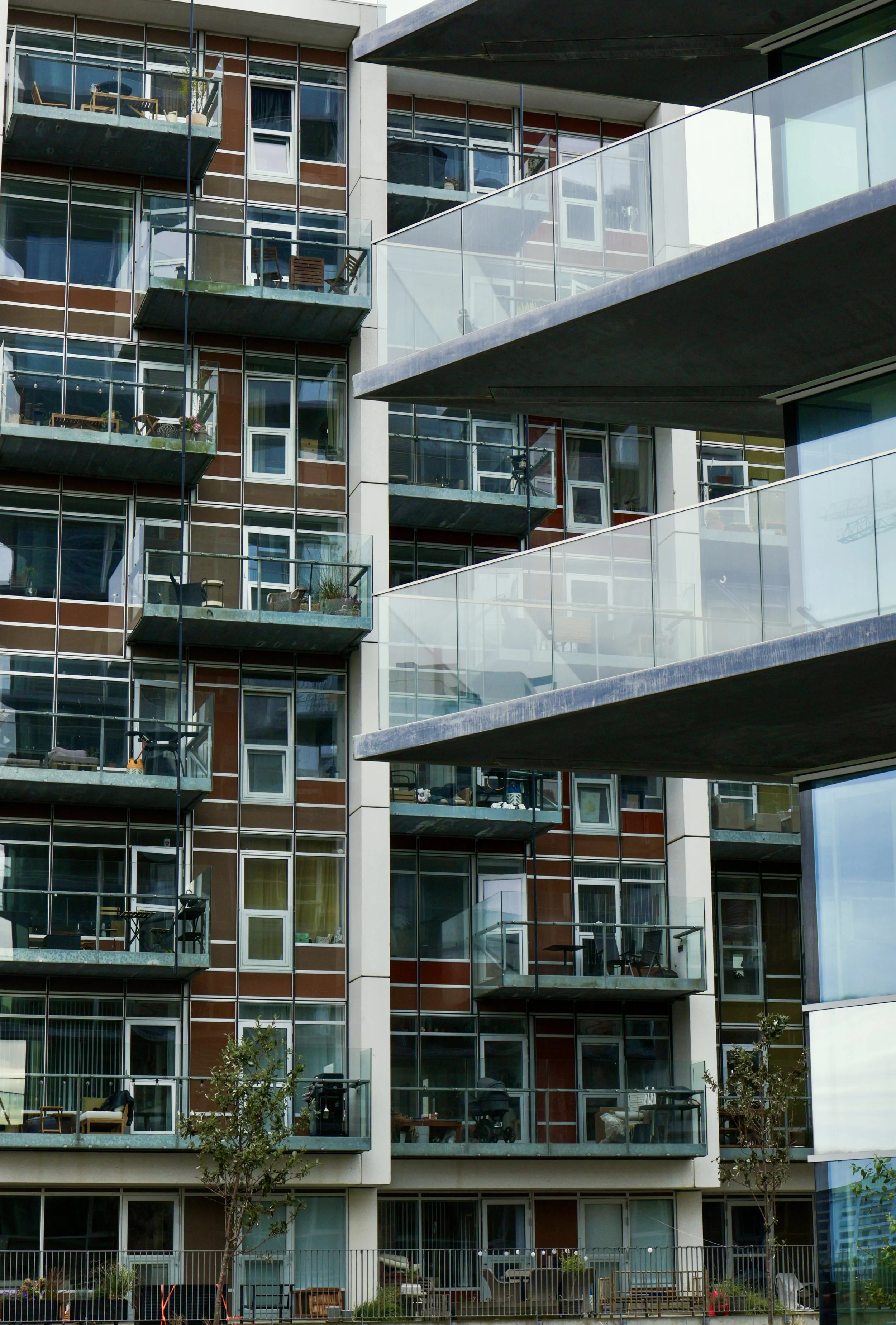 Facade of a modern apartment building with glass balconies and visible interior furnishings.