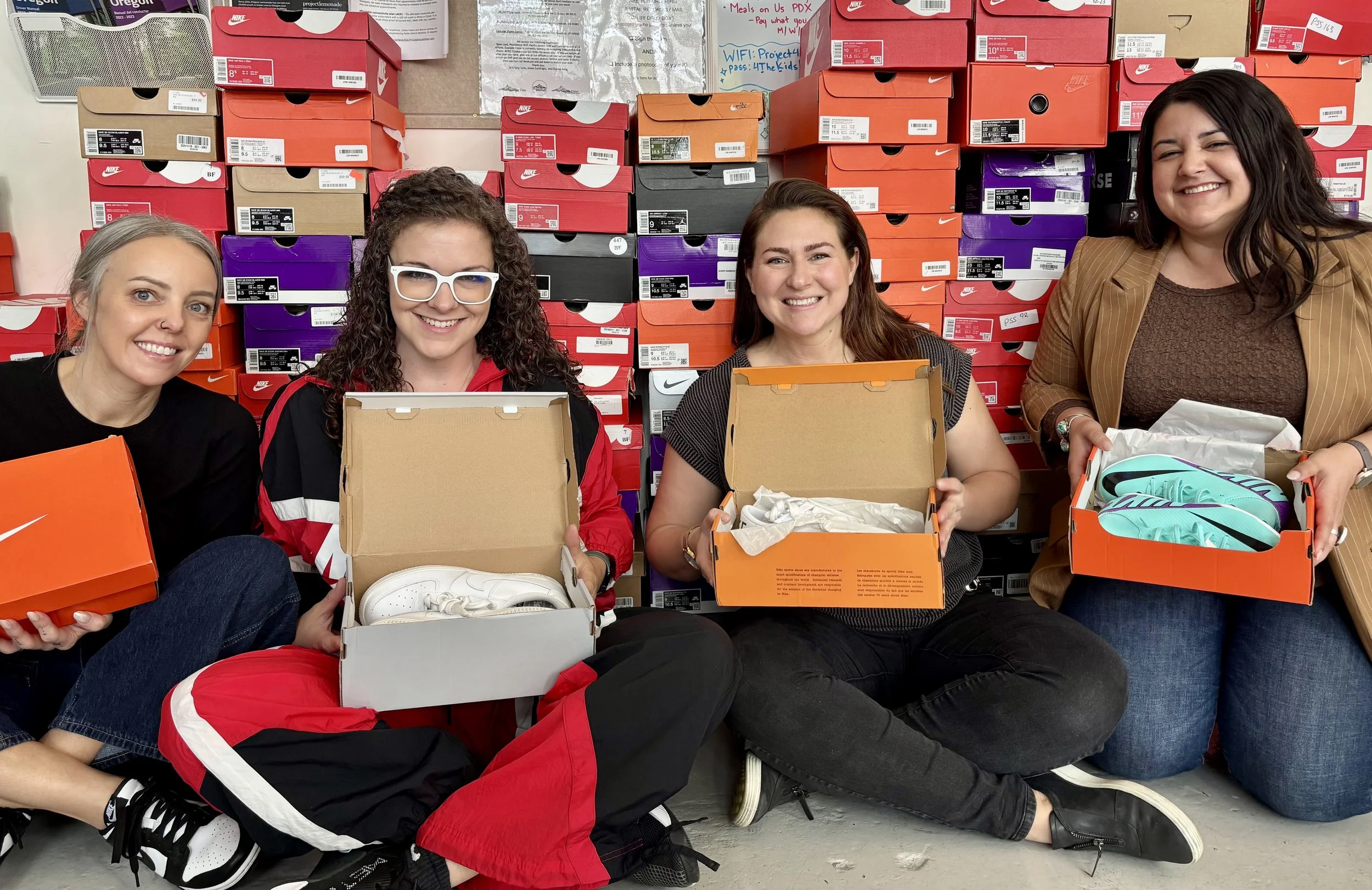 Two women holding shoe boxes with shoe boxes behind them.