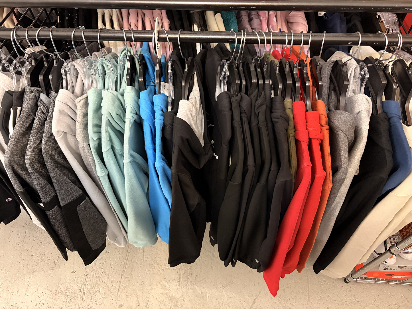 Clothing rack with hoodies in various colors including gray, mint green, blue, black, red, orange, and beige.