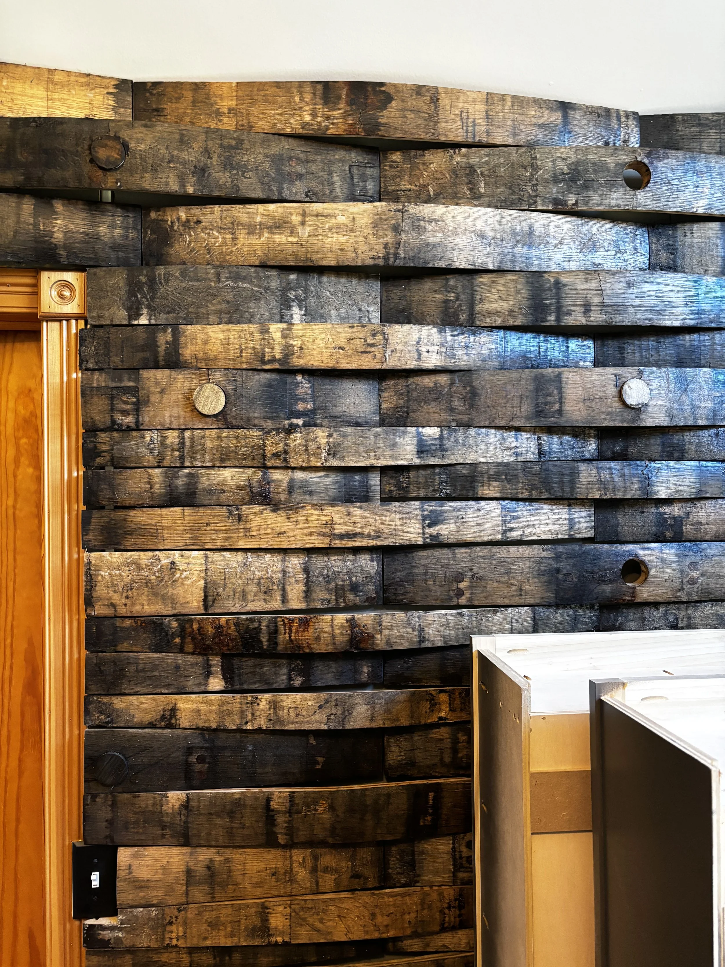A wall with dark, weathered wooden planks, some with visible round metal nails, and a section of light-colored wood furniture partially visible on the right side.