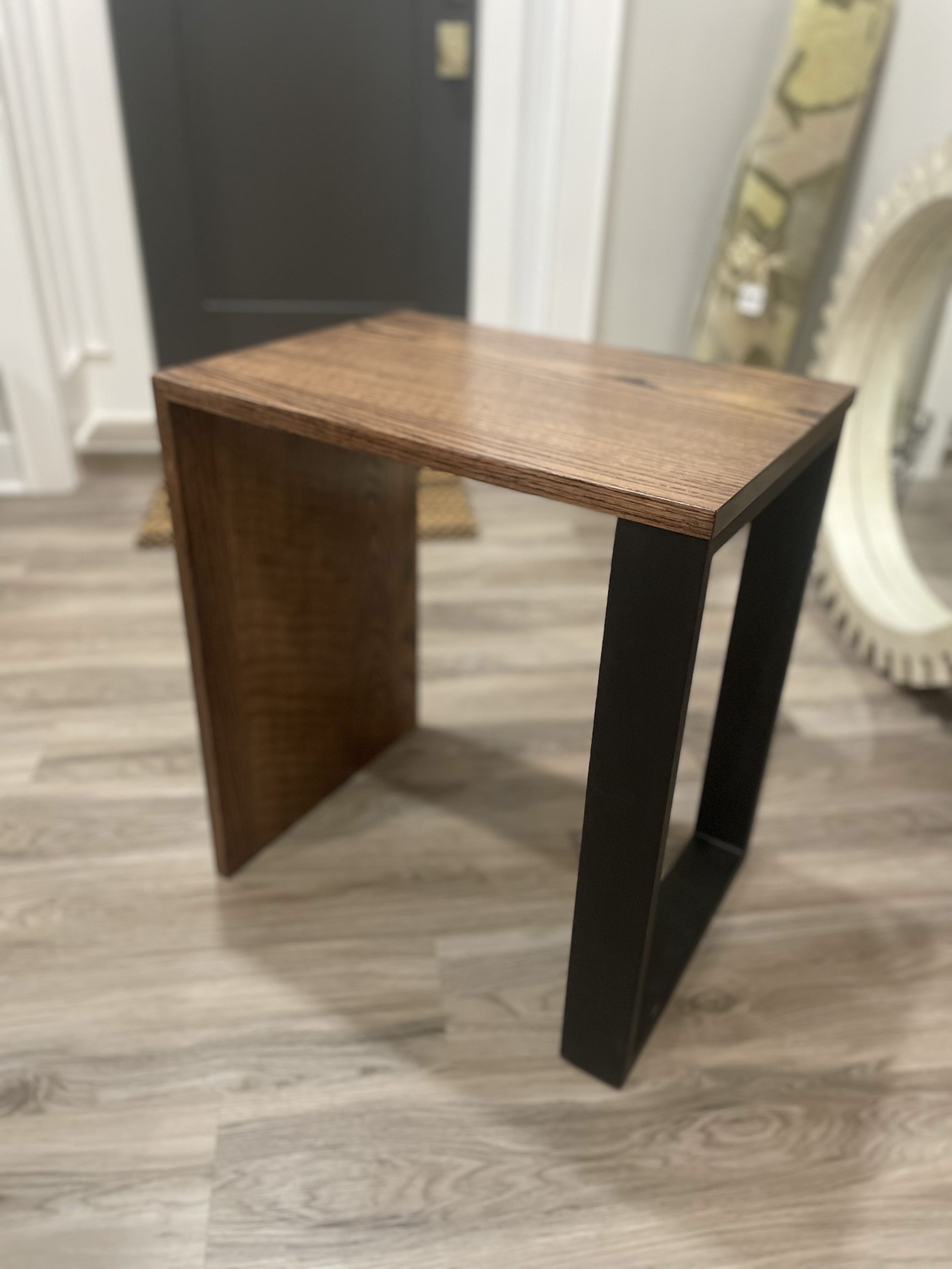 Close-up of a modern piece of furniture combining a wooden top and black metal legs, set on a light-colored wood floor.