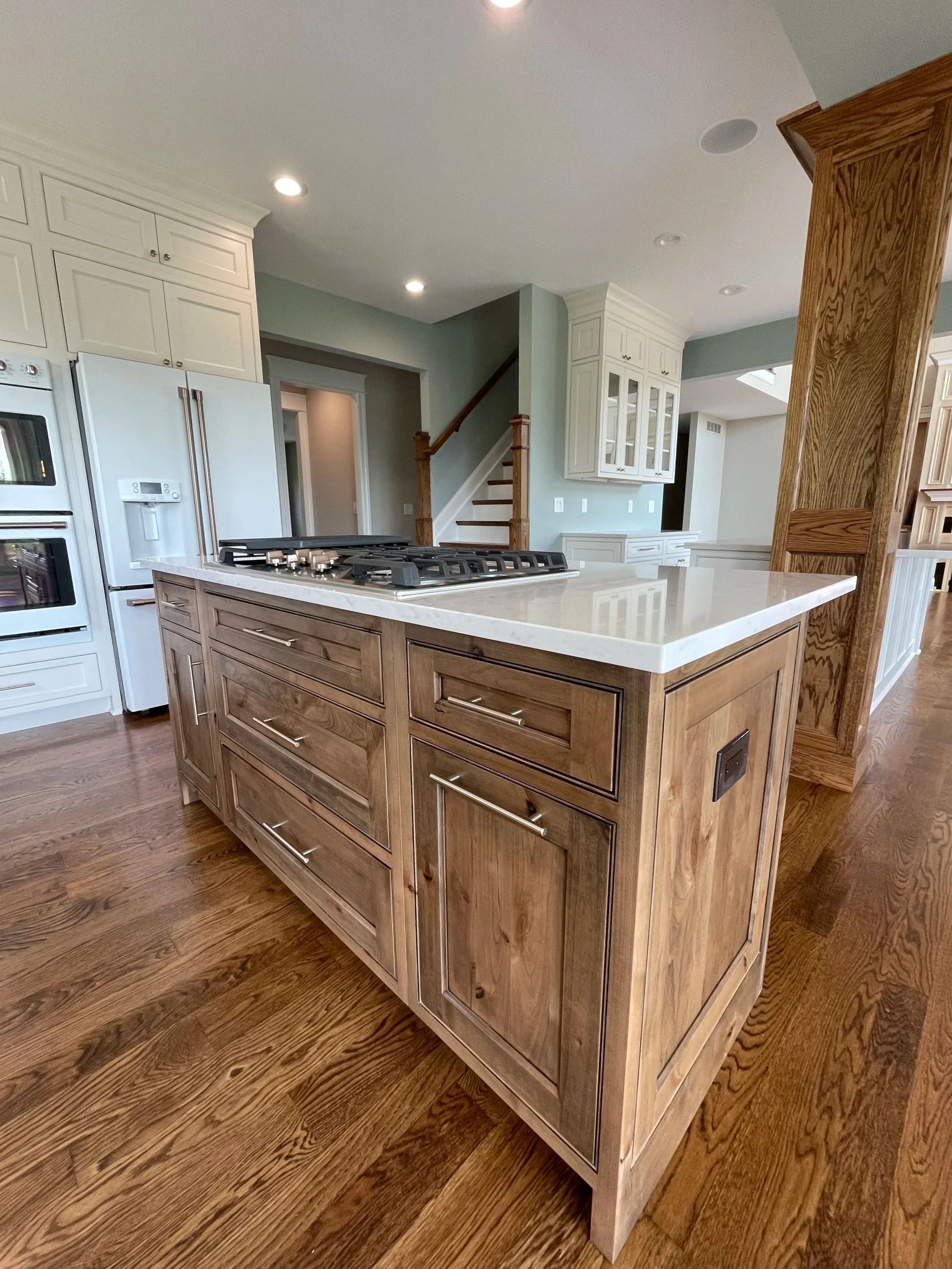 Modern kitchen with white cabinets, a large island with a wooden finish, and hardwood flooring.