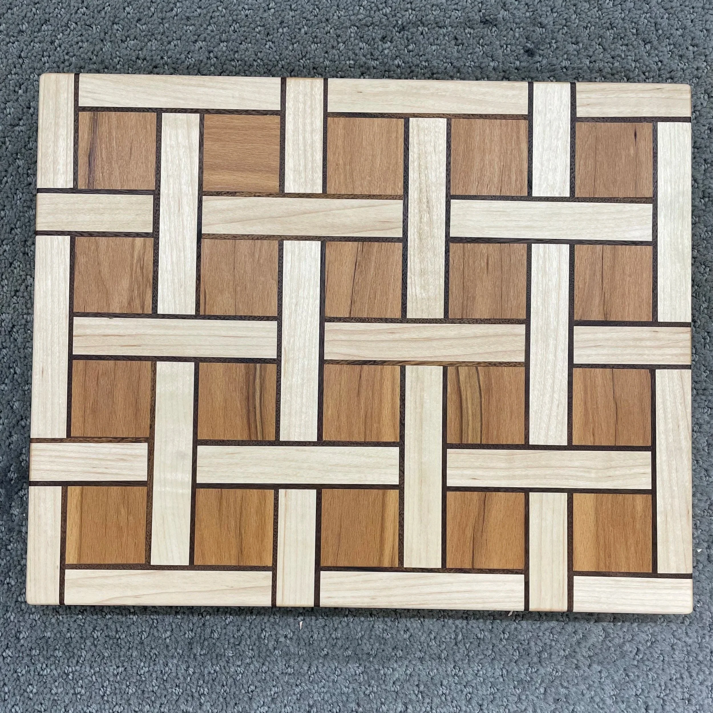 A wooden checkerboard with alternating light and dark wooden squares, placed on a gray carpeted surface.