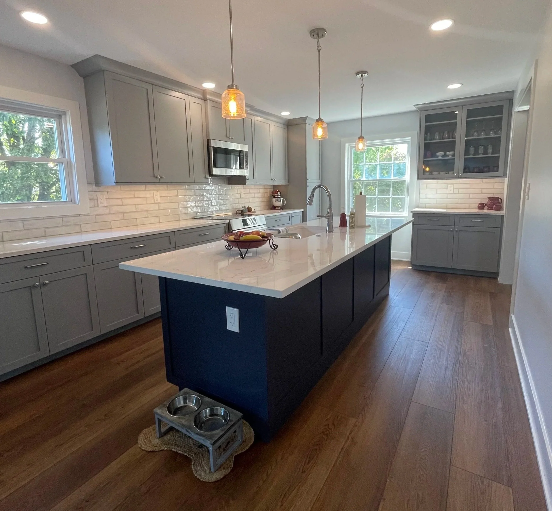 Modern kitchen with gray cabinets, white subway tile backsplash, a kitchen island with a white countertop, pendant lights, and hardwood flooring.