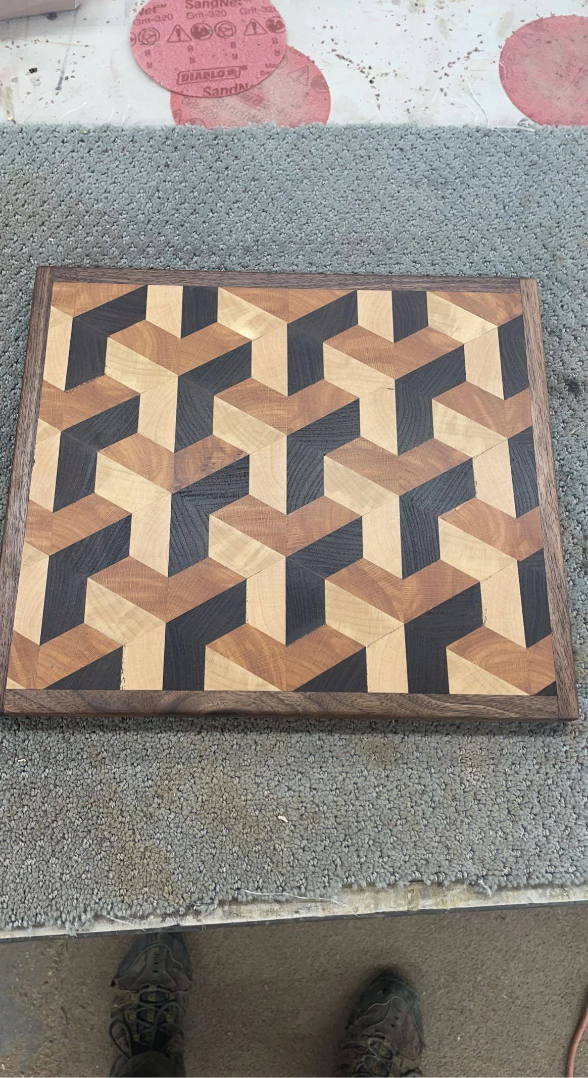 Close-up of a geometric wooden chessboard with an intricate pattern of three-dimensional cubes, placed on a textured gray surface.