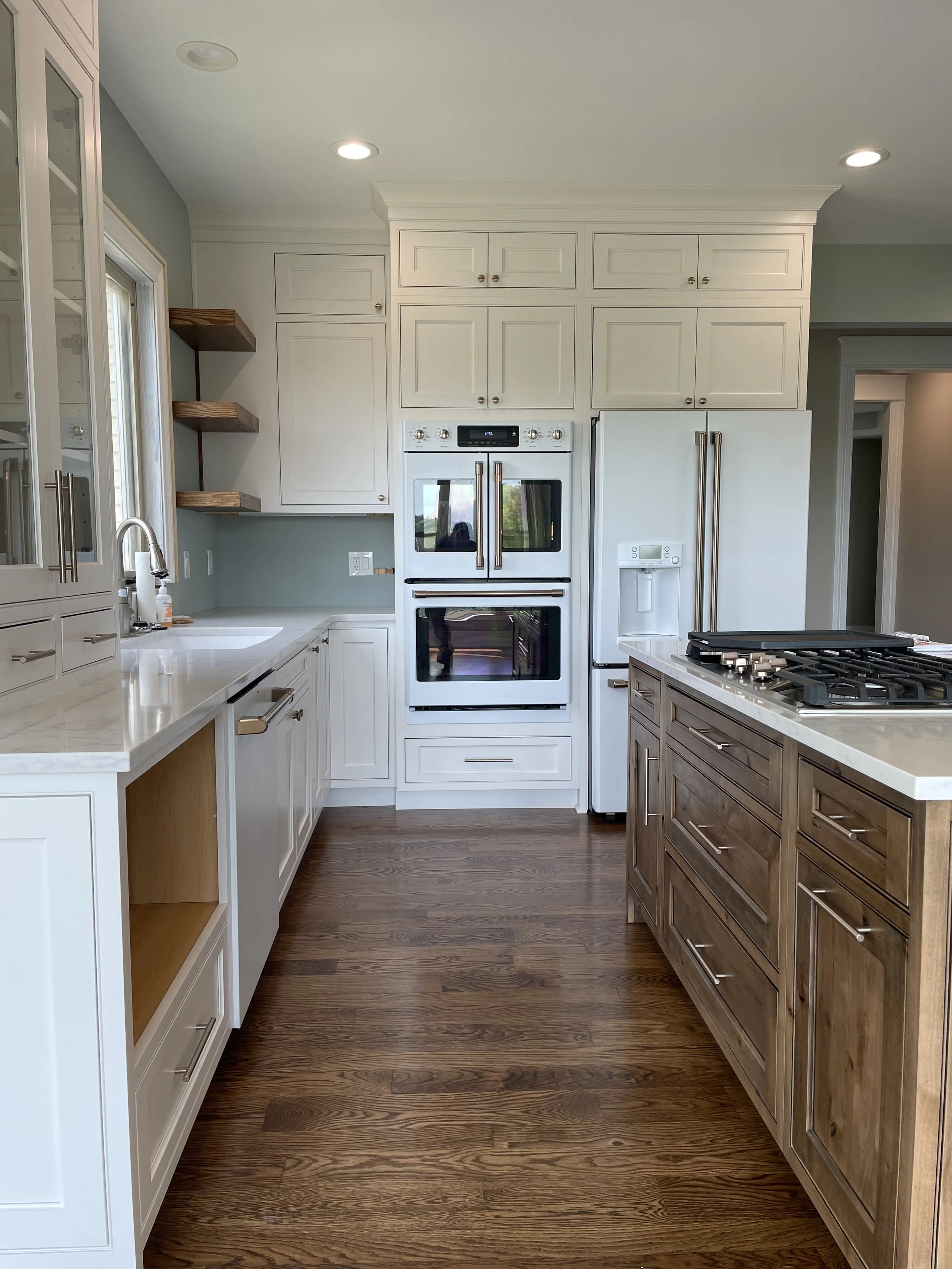A modern kitchen with white and wooden cabinets, a double oven, a countertop with a sink, wooden floor, and recessed lighting.