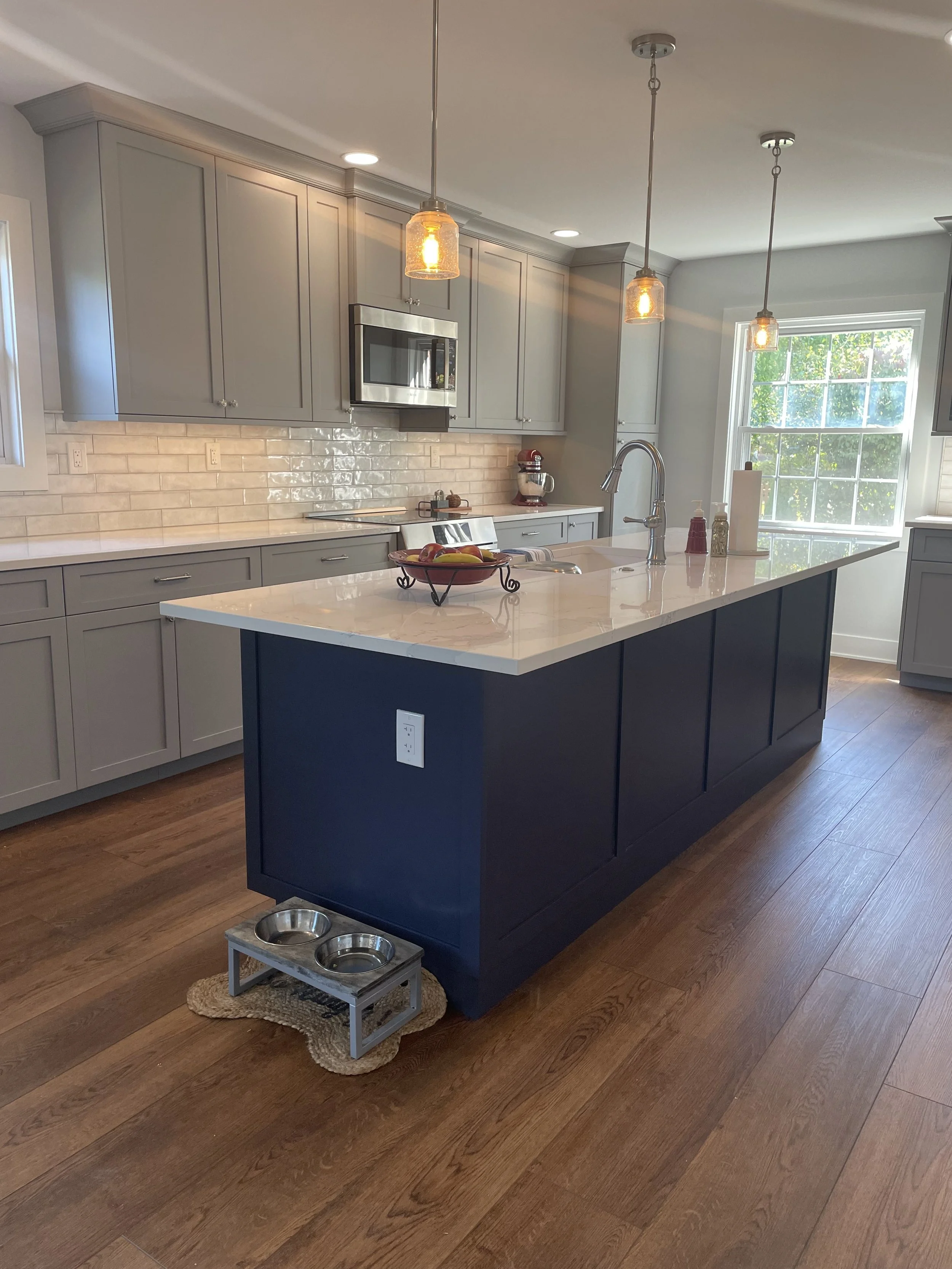 Modern kitchen with gray cabinets, white marble island, pendant lights, and a window letting in natural light.
