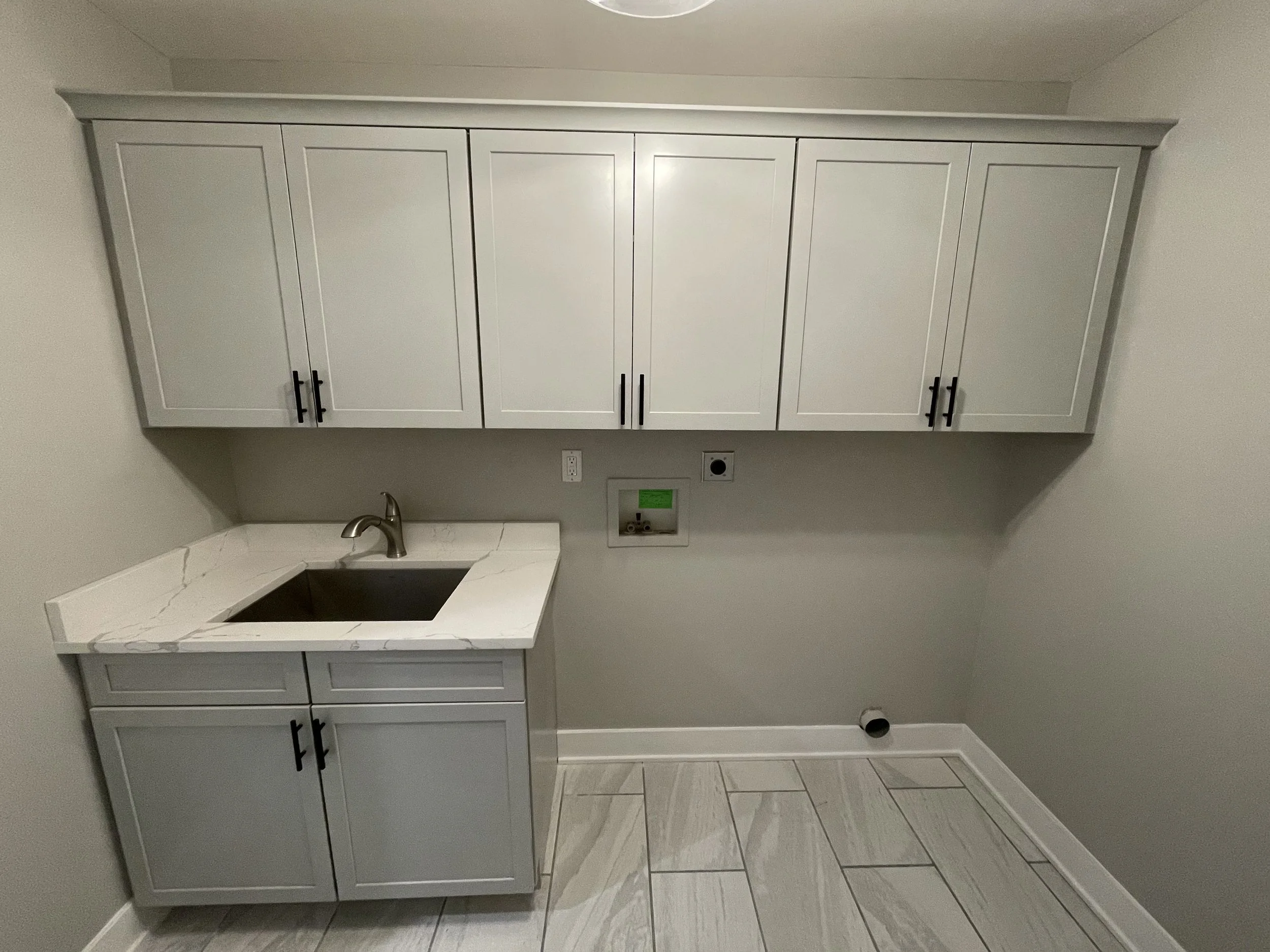 A gray kitchen cabinet with black handles, a white countertop, a stainless steel faucet, and a gray tiled floor.