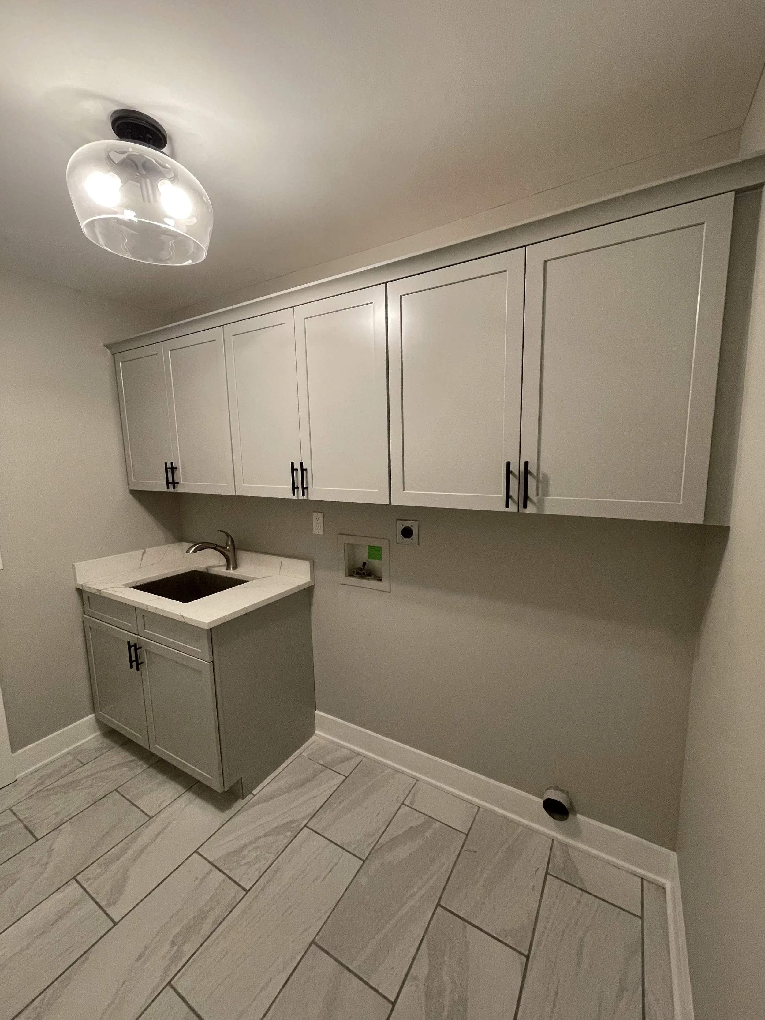 Empty laundry room with gray cabinets, a small sink, and a tiled floor.