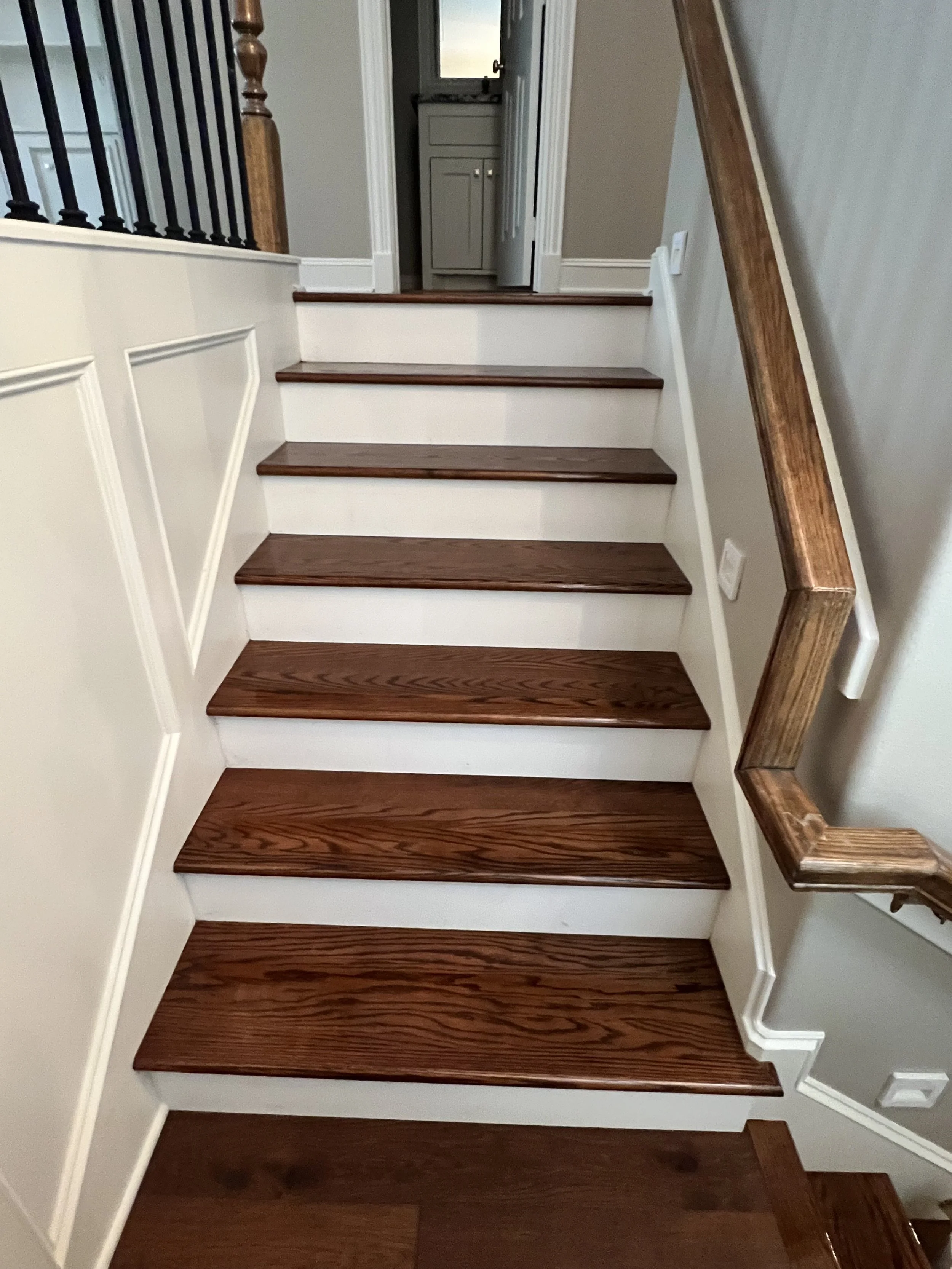 Wooden stairs with white risers and a wooden handrail on the right, leading to a small landing and a doorway into another room, with a window above the doorway.