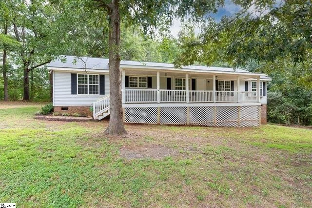 Single-story house with a large front porch, white railing, and white siding, surrounded by trees and grass.