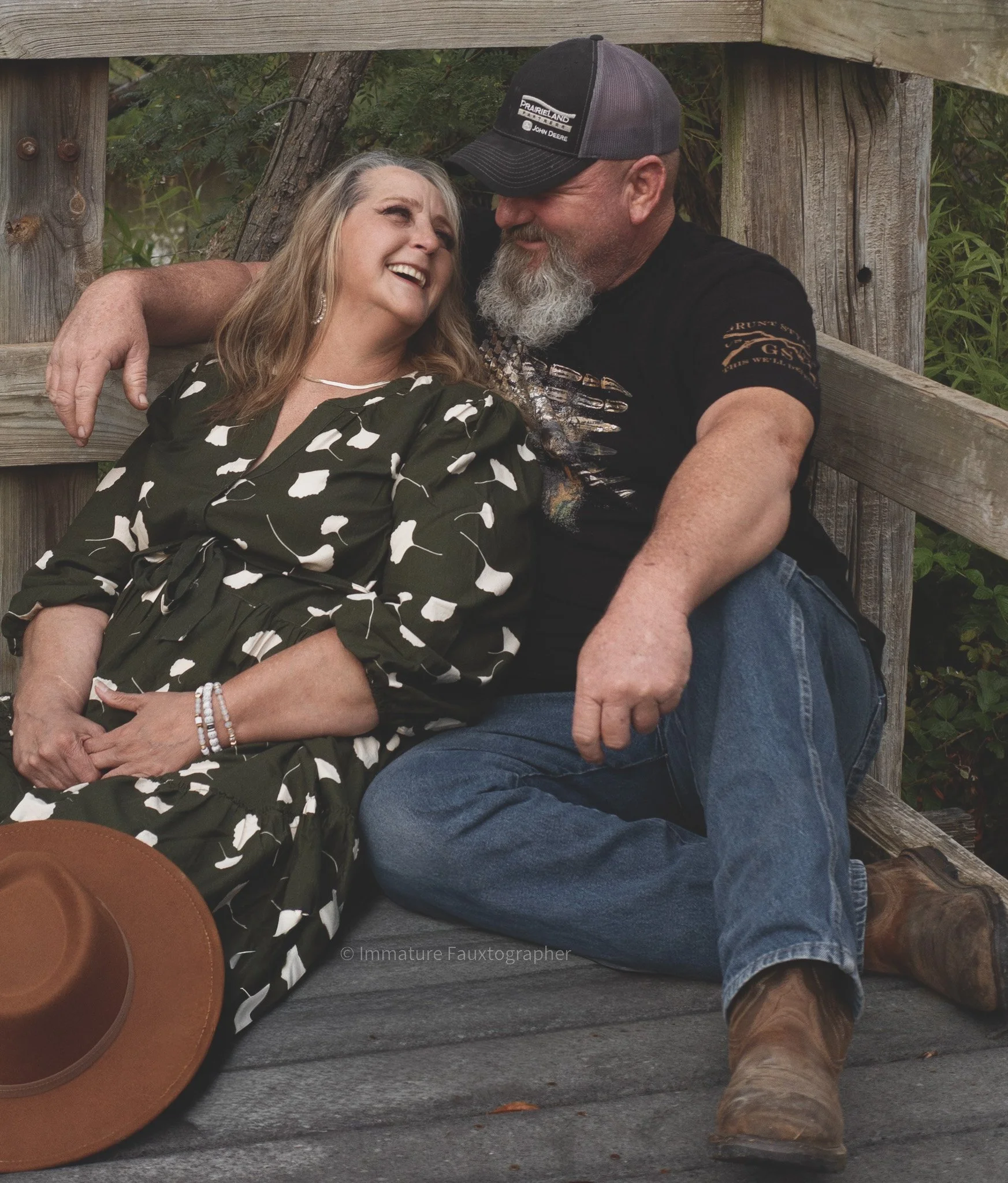 A middle-aged couple sitting on a wooden bench outdoors, sharing a joyful moment, smiling and looking into each other's eyes.