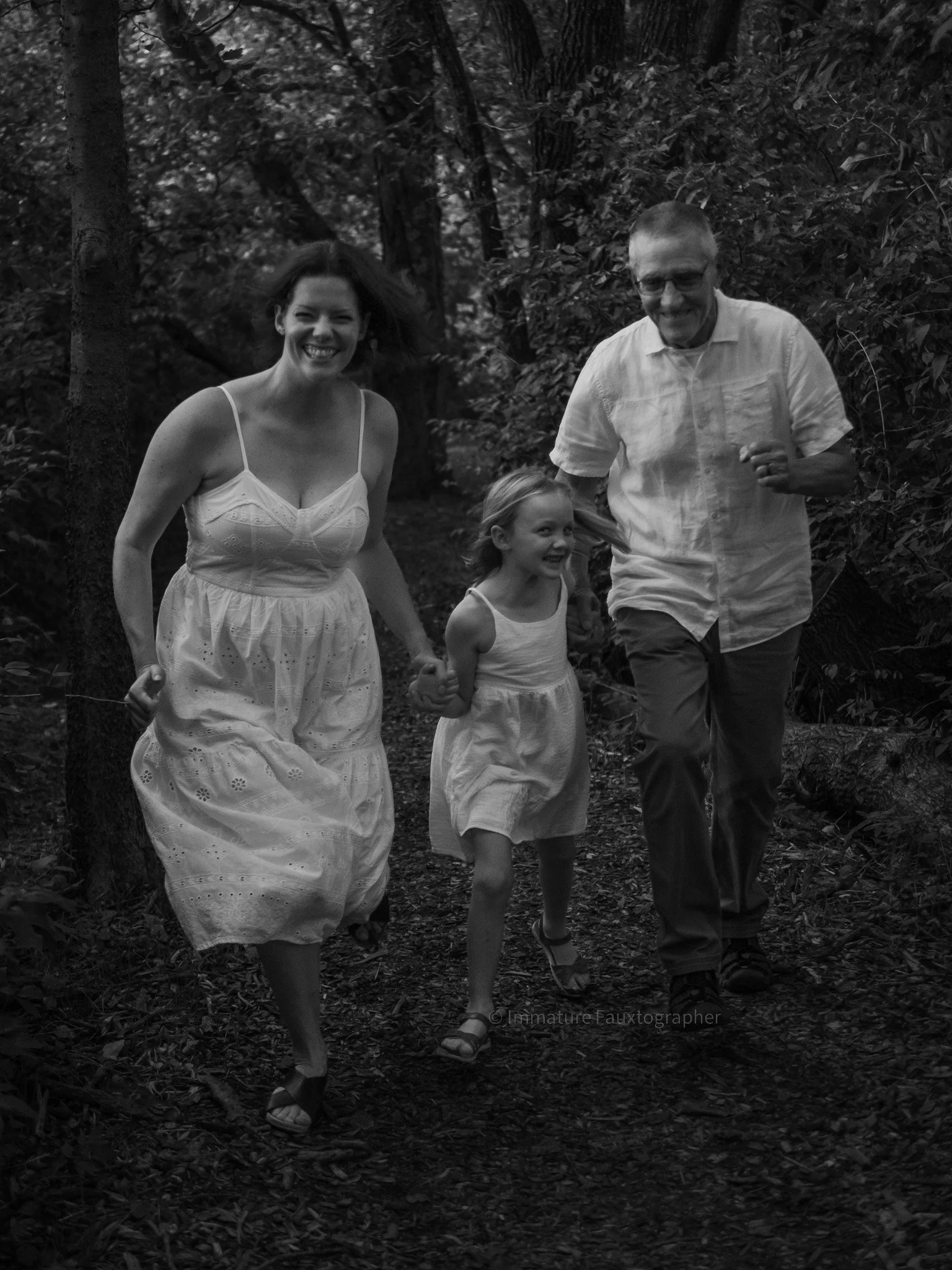 A family of three, including a woman, a man, a young girl, running and smiling along a wooded path.