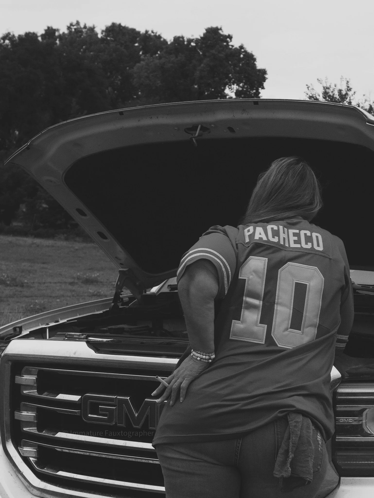 A woman wearing a sports jersey with the name 'Pacheco' and the number 10, standing at a GMC vehicle with its hood open in an outdoor setting.