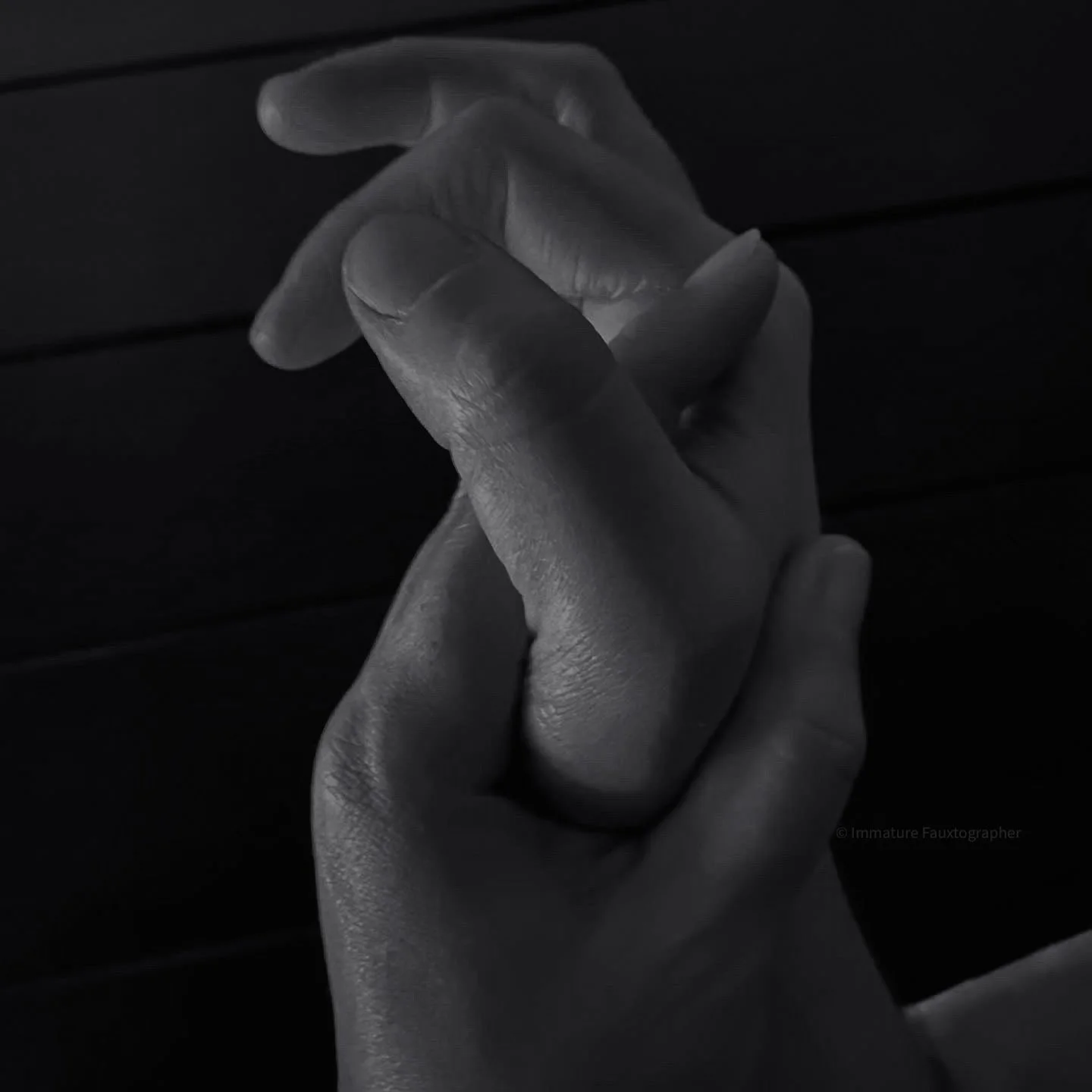 Black and white photo of a person's hand with fingers intertwined, resting against a dark surface.