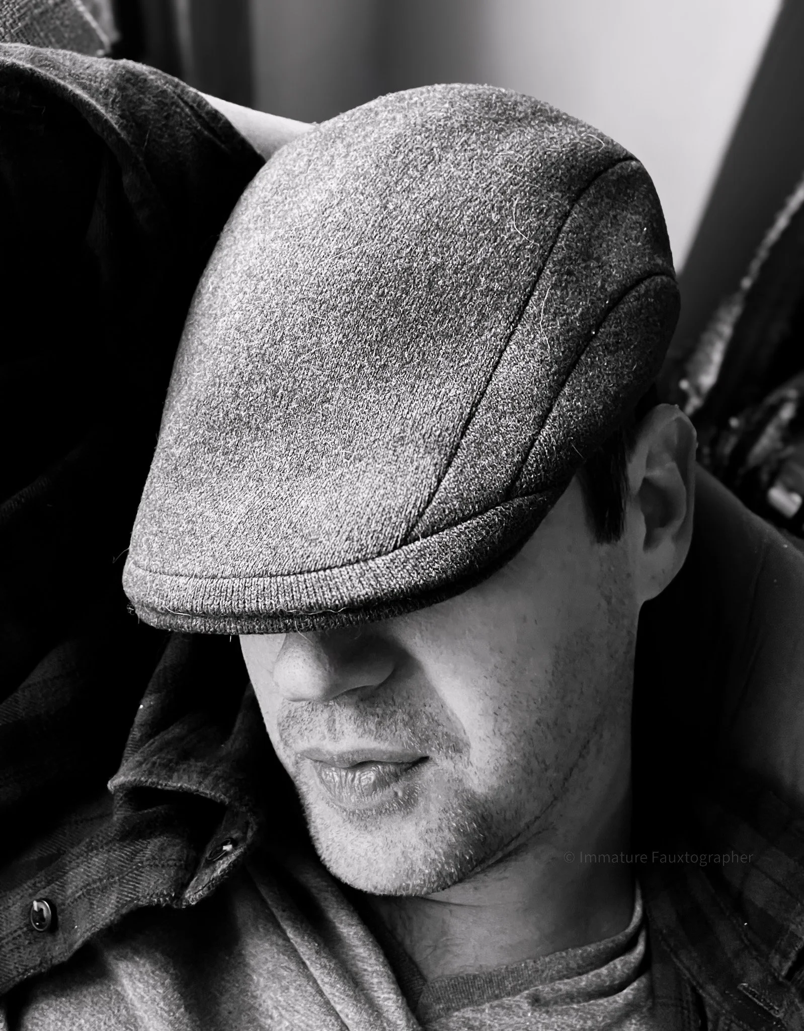 A man with a cap pulled low over his eyes resting his head on his arm and a slight smile on his mostly covered face.