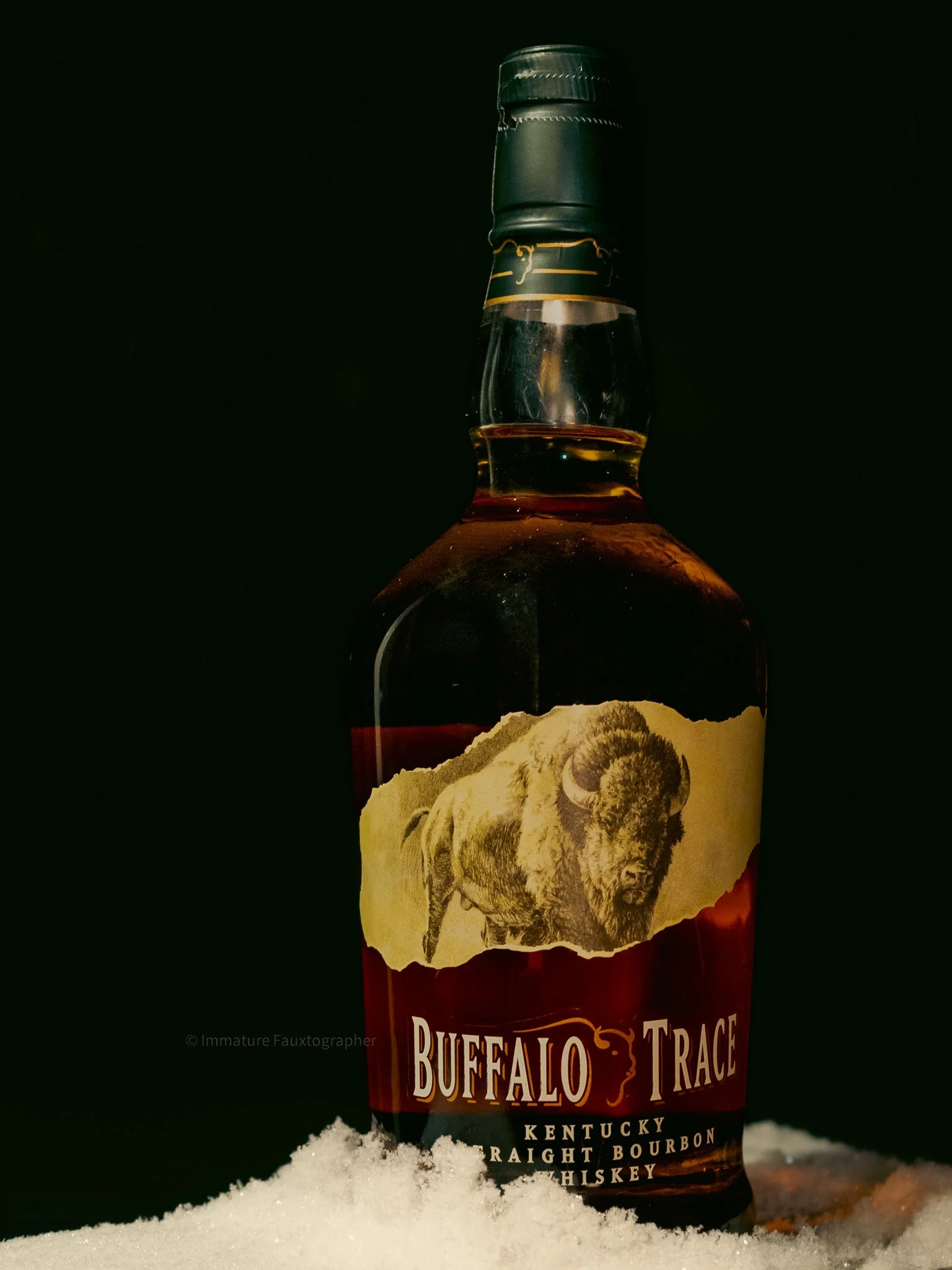 A bottle of Buffalo Trace Kentucky Straight Bourbon Whiskey placed on snow with a dark background.