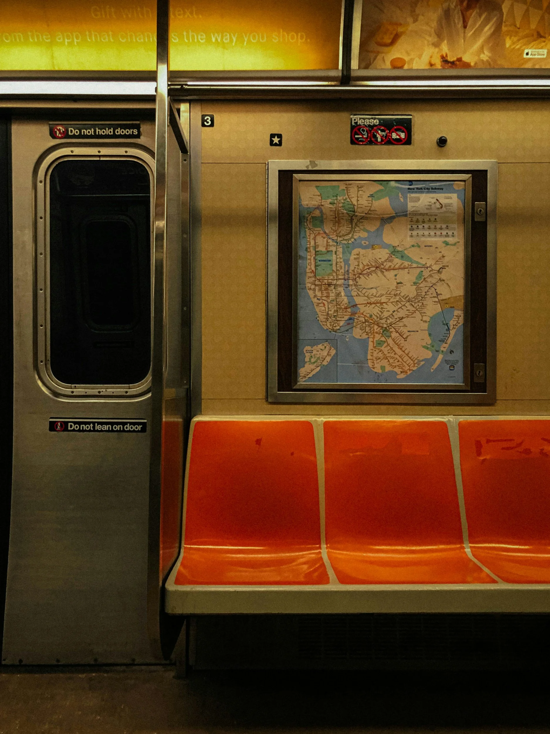 Empty orange subway station bench next to a map of the New York City Subway and a device to pay fares, with signs signaling not to hold doors and not to lean on door.