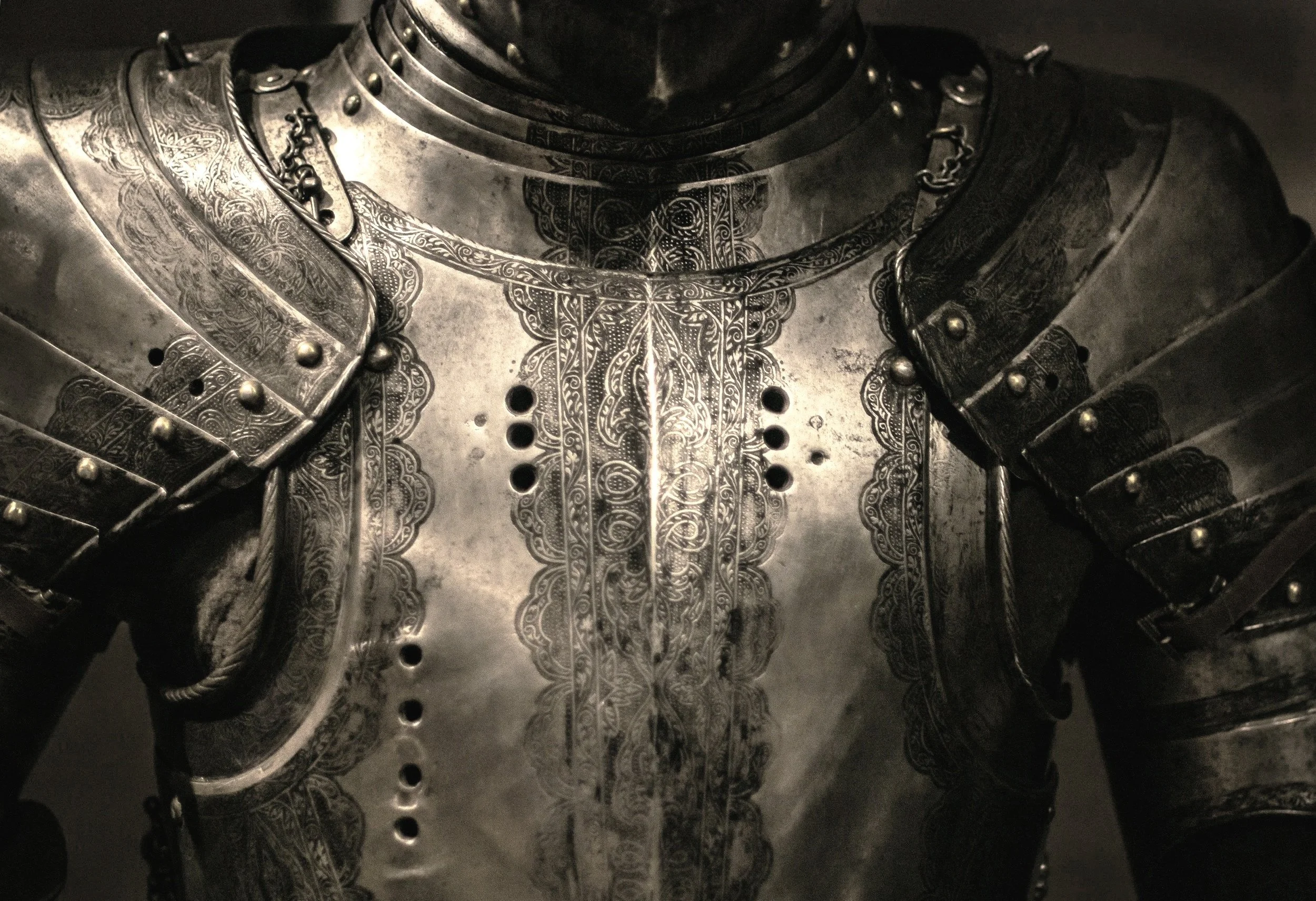 Close-up of a silver suit of armour, showing detailed engravings and metal plates.