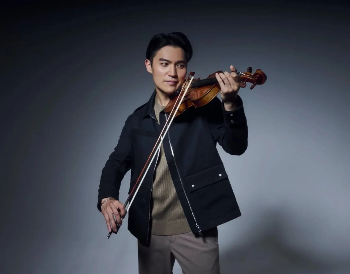 A man playing a violin against a dark gray background.
