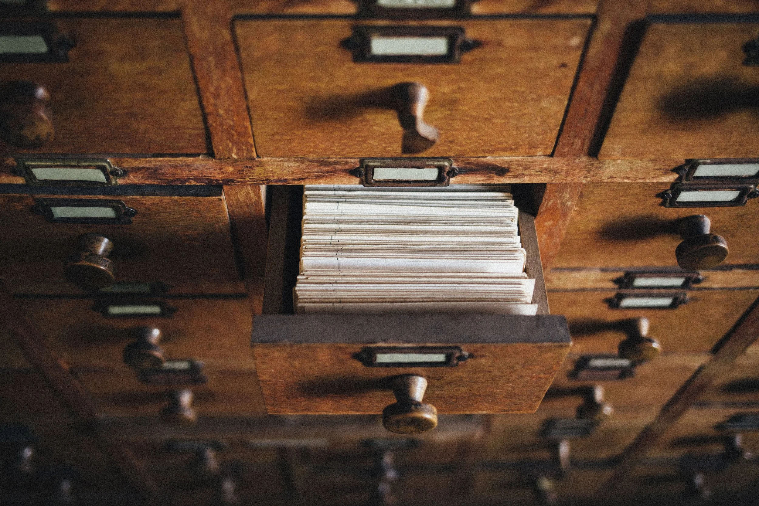 Open drawer of a wooden filing cabinet filled with neatly stacked vintage paper files.